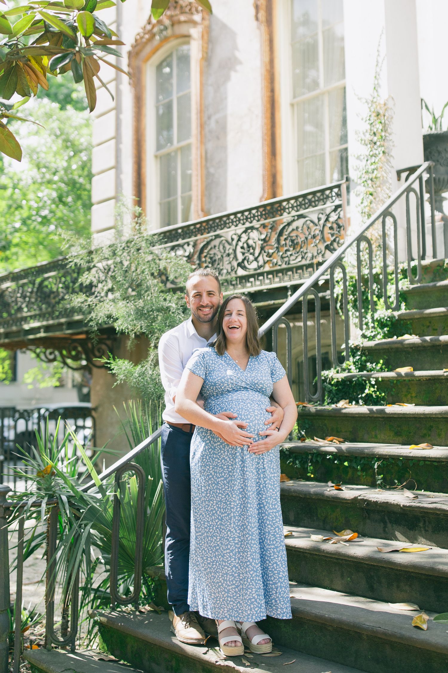 Couple shares intimate moment on garden steps with ornate iron railing and greenery in background.