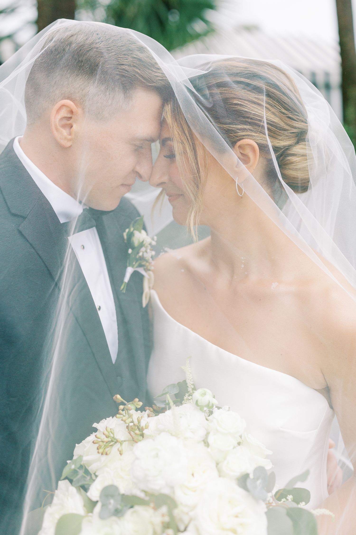 Romantic wedding portrait through a delicate veil with white floral bouquet.