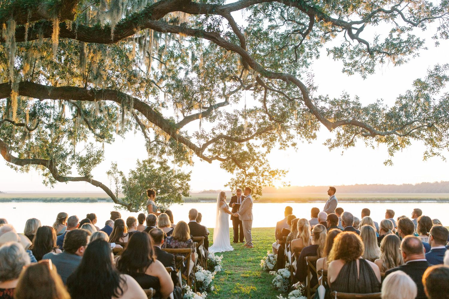 Sunset wedding ceremony under grand oak tree with Spanish moss overlooking waterfront at Beaulieau.