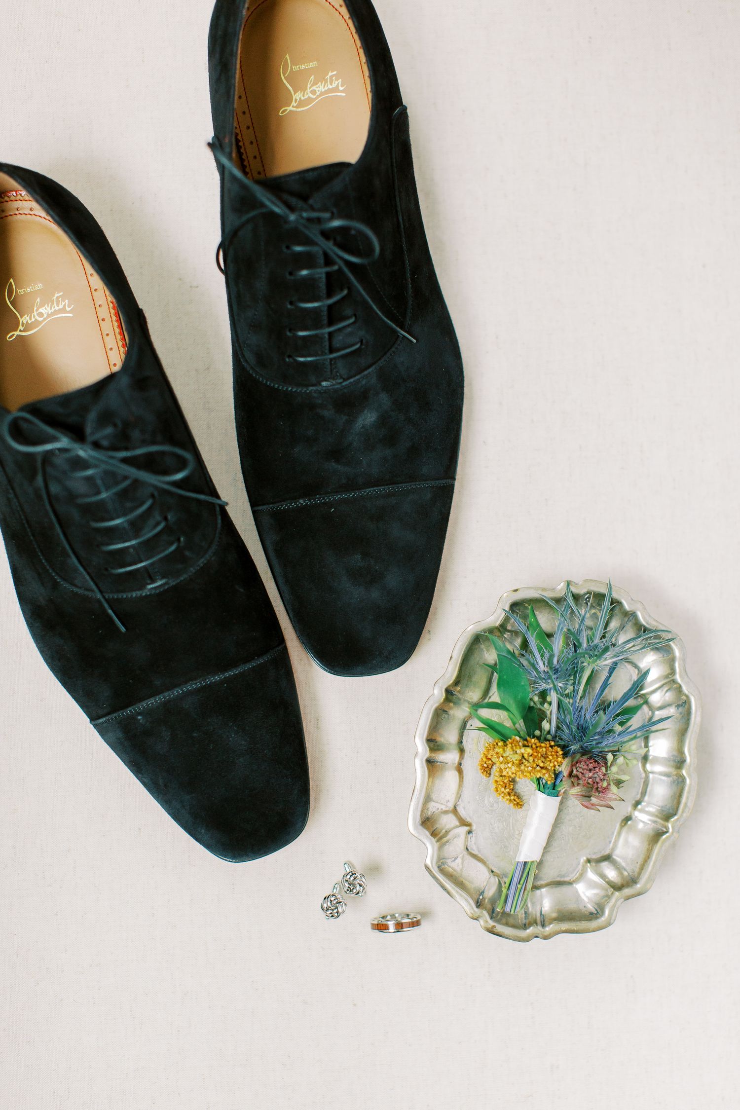 Navy blue suede oxford dress shoes displayed alongside a decorative glass dish and small jewelry pieces.