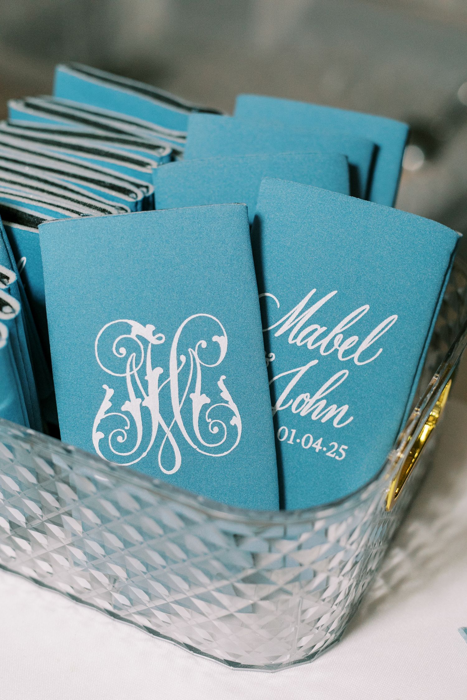 Turquoise wedding favor koozies with white monograms and dates arranged in display.
