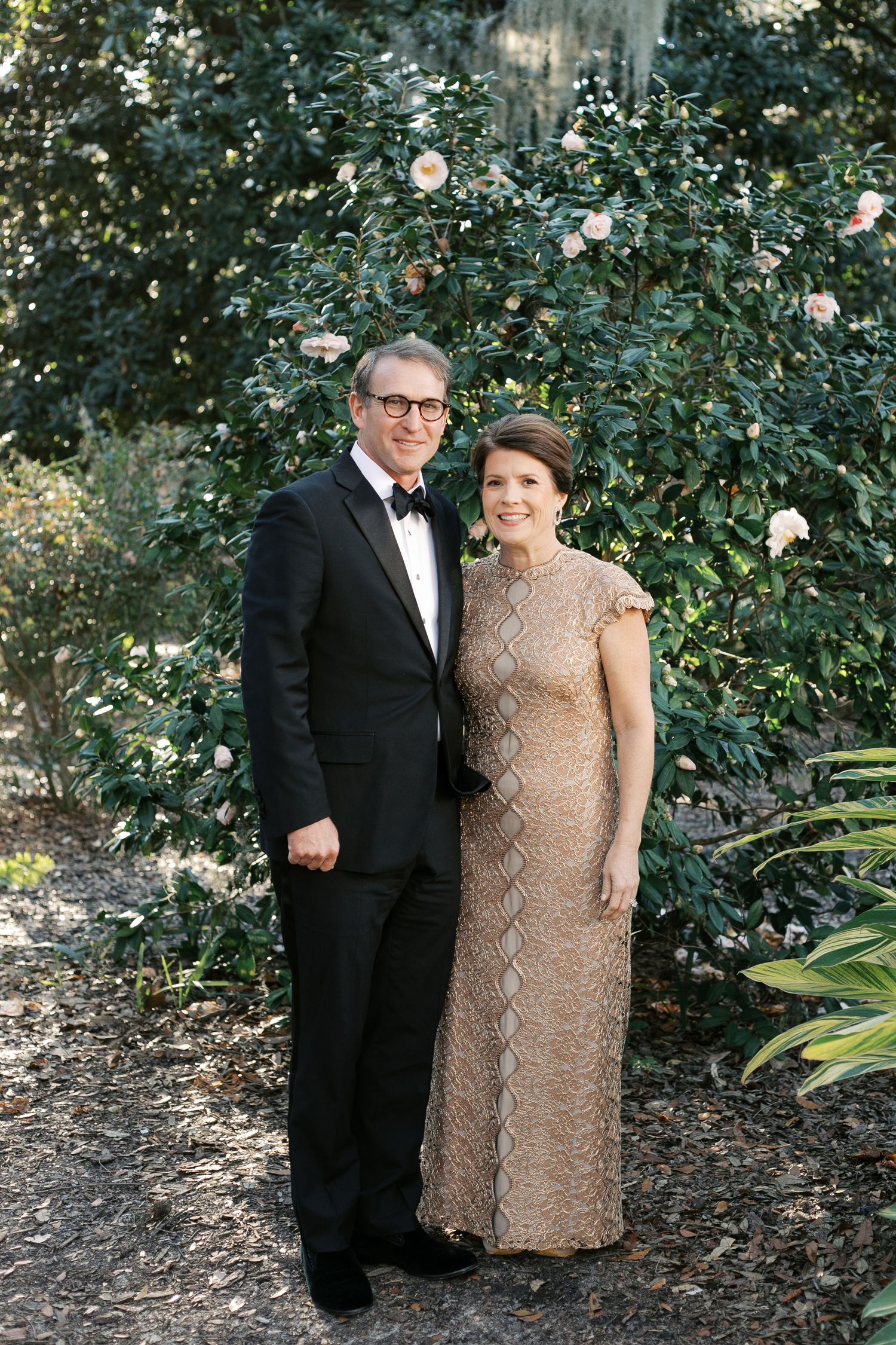 Formal portrait in garden setting with evening attire against floral backdrop.