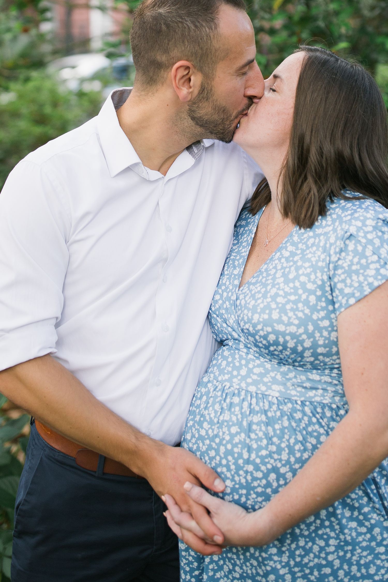 A romantic sequence of a couple embracing and kissing while wearing coordinating outfits in a garden setting during a maternity session.