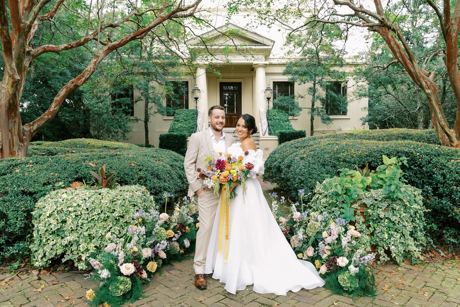 Wedding party in white dresses poses together in a lush garden setting decorated with colorful spring flowers.