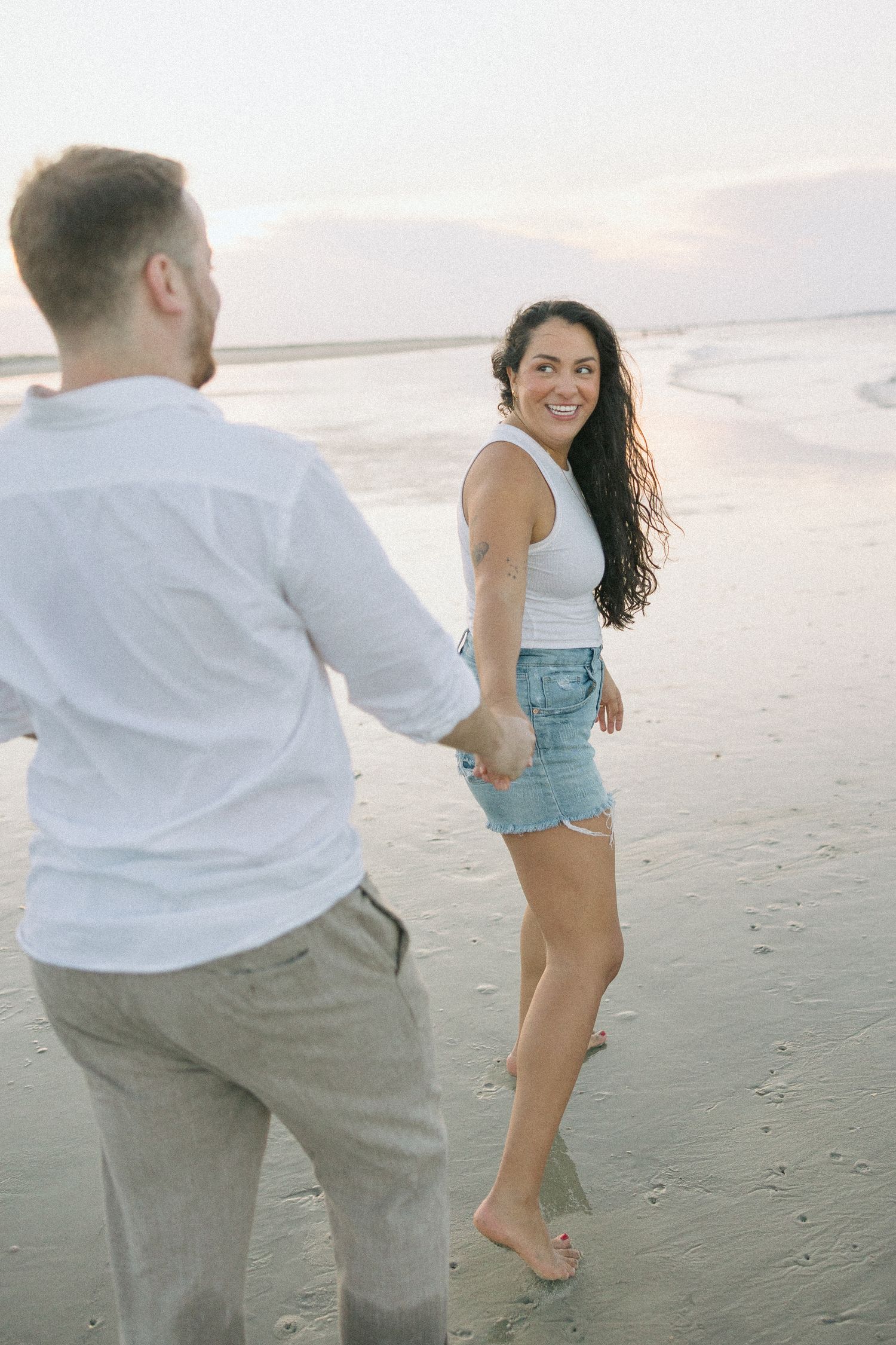 Couple playfully chasing each other on a sandy beach at sunset, creating a romantic atmosphere.