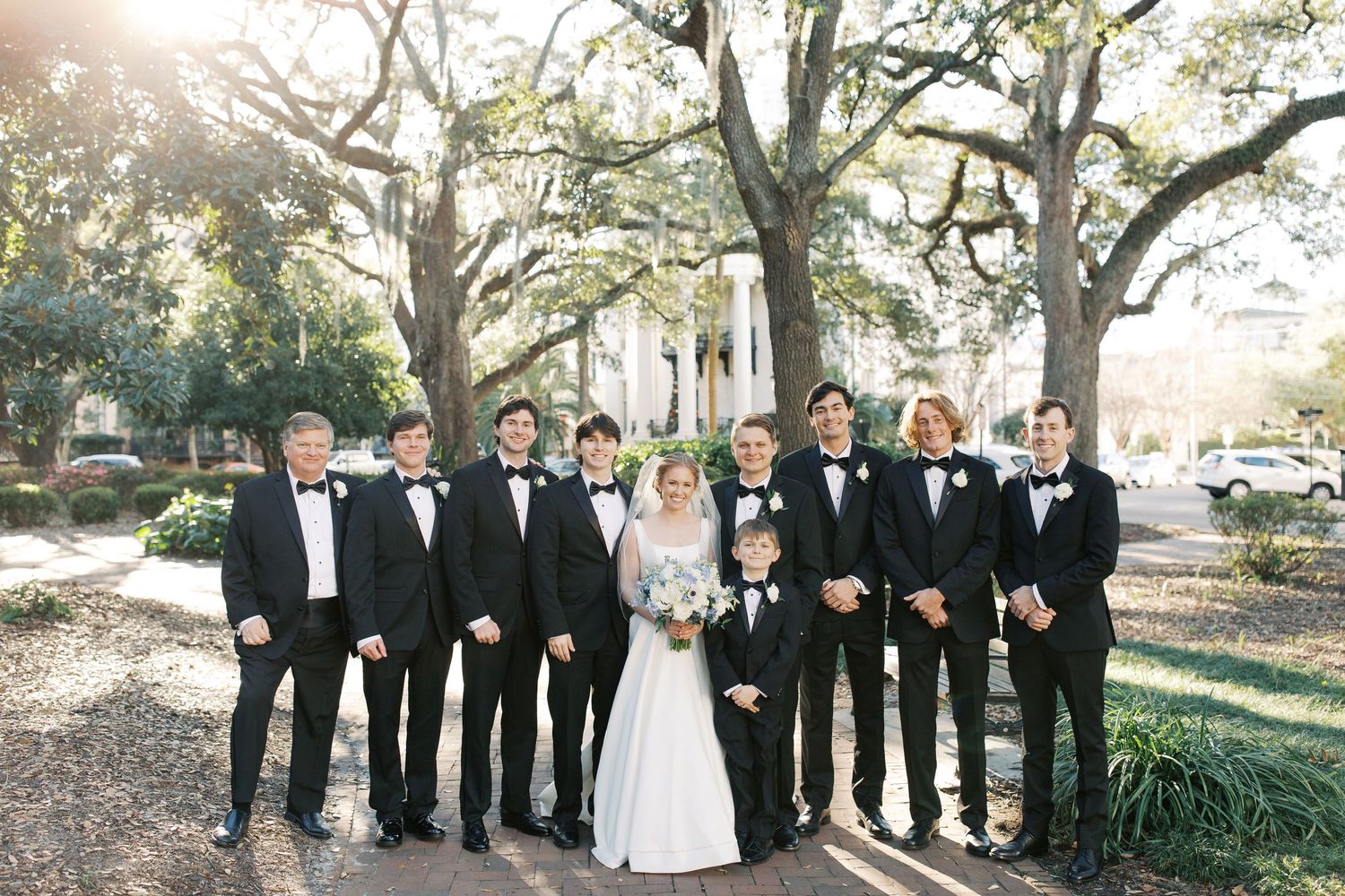 Wedding party poses outdoors under large oak trees draped with Spanish moss in natural lighting.