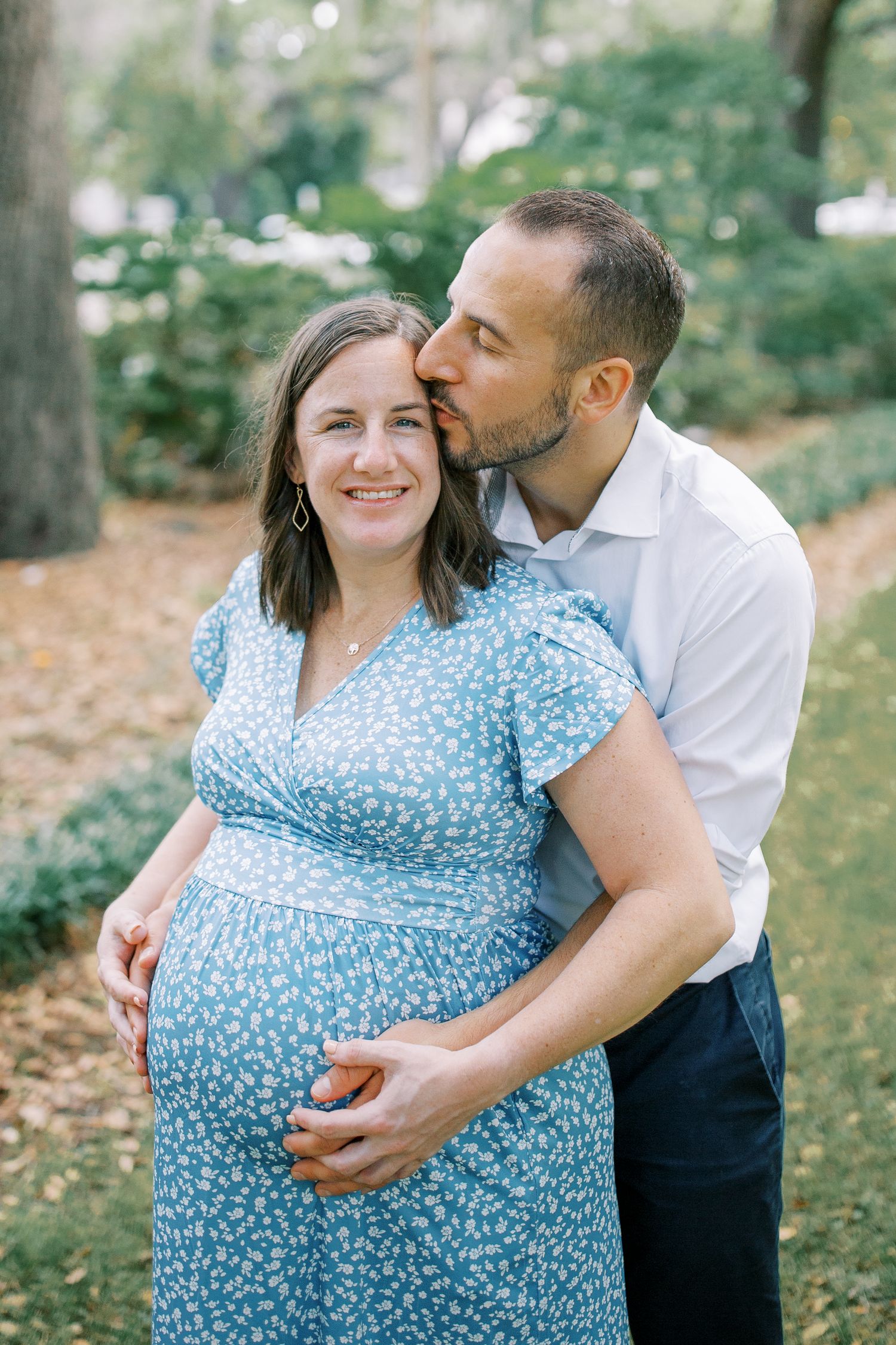 Loving couple embraces during maternity photo session in a garden setting.