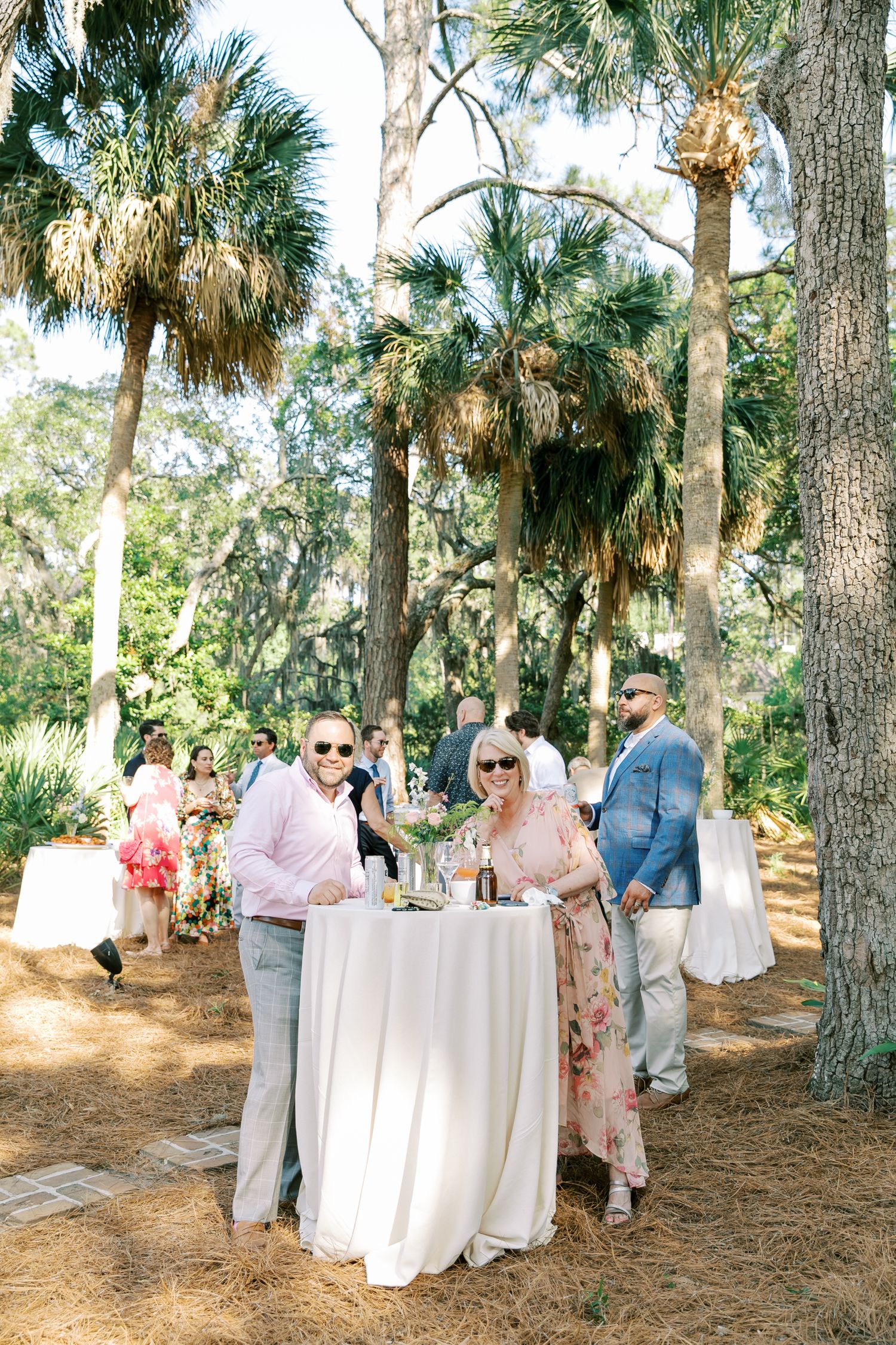 Guests gather around cocktail tables under palm trees at an elegant outdoor wedding reception.