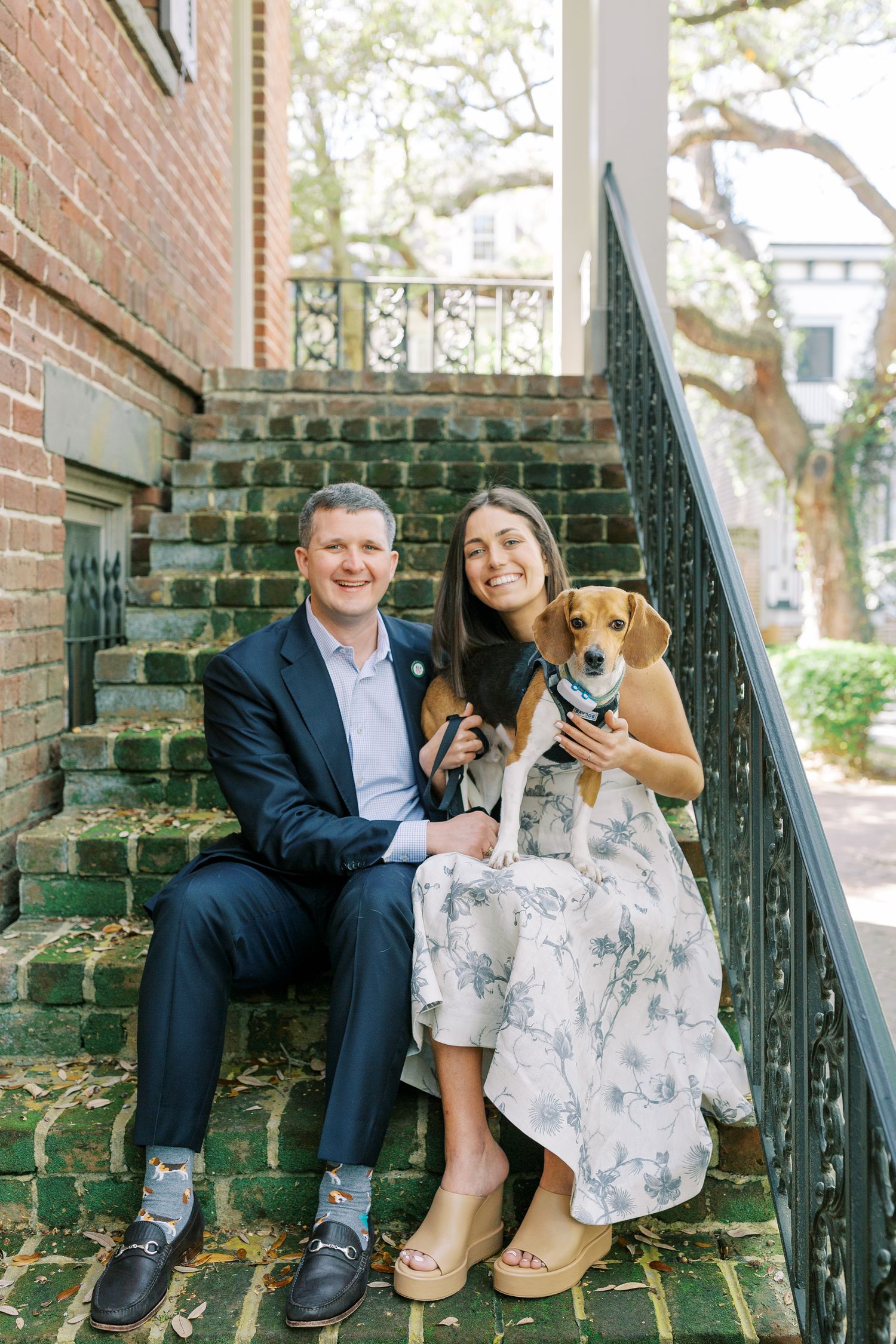 A couple sits together on brick steps of a historic downtown Savannah home with their small Jack Russell terrier dog.