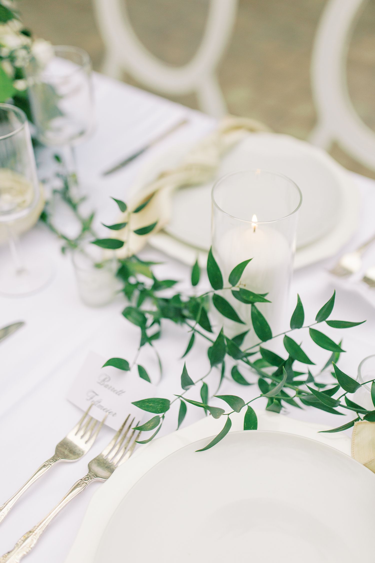 Minimalist table setting with white plates, greenery garland, and glowing candle.