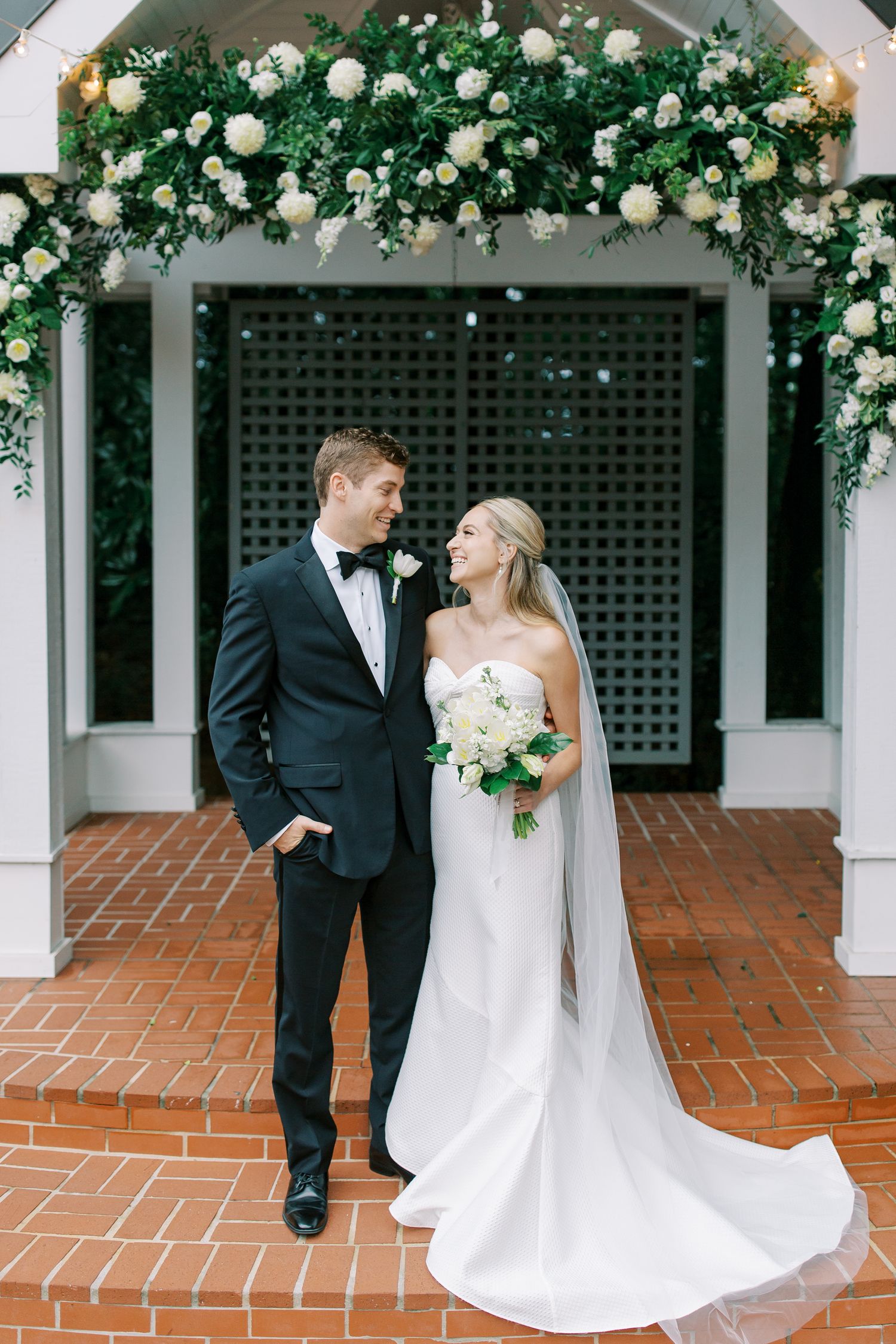 Elegant wedding portrait under floral arch with white roses and greenery.