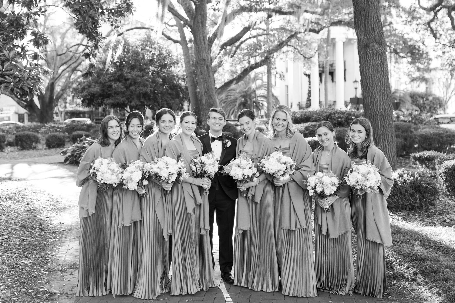 Wedding party arranged in a long line outdoors with bridesmaids wearing matching gray dresses.