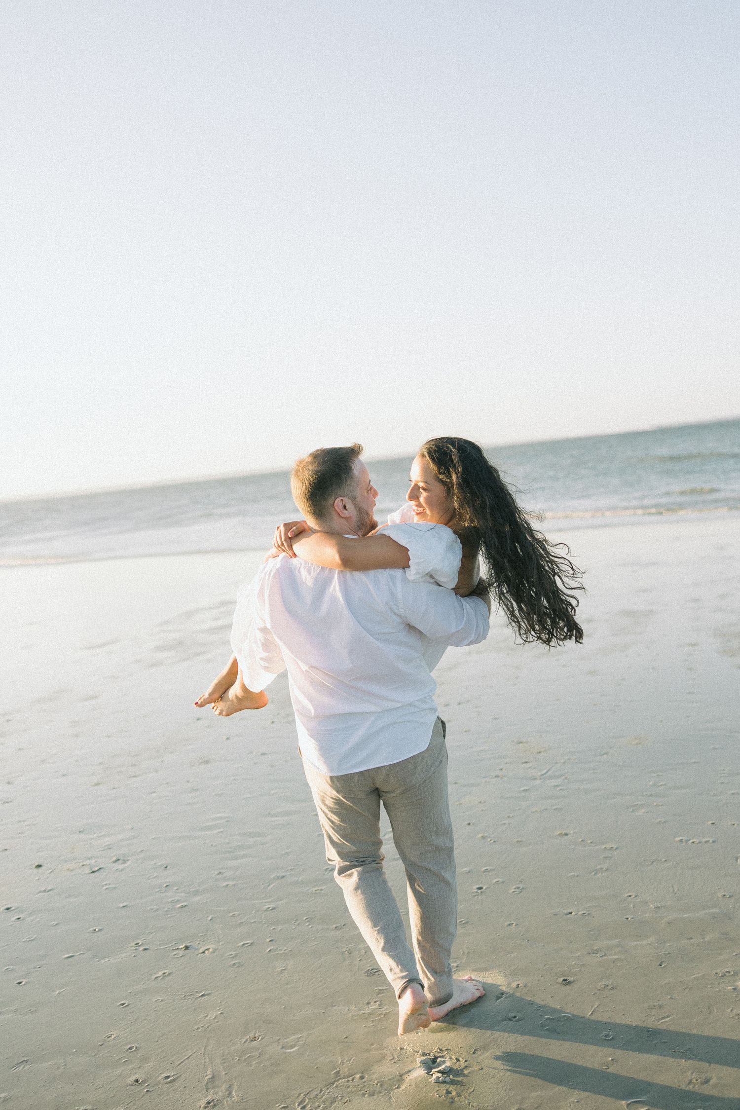 Couple dancing and spinning together on an empty beach at sunset.