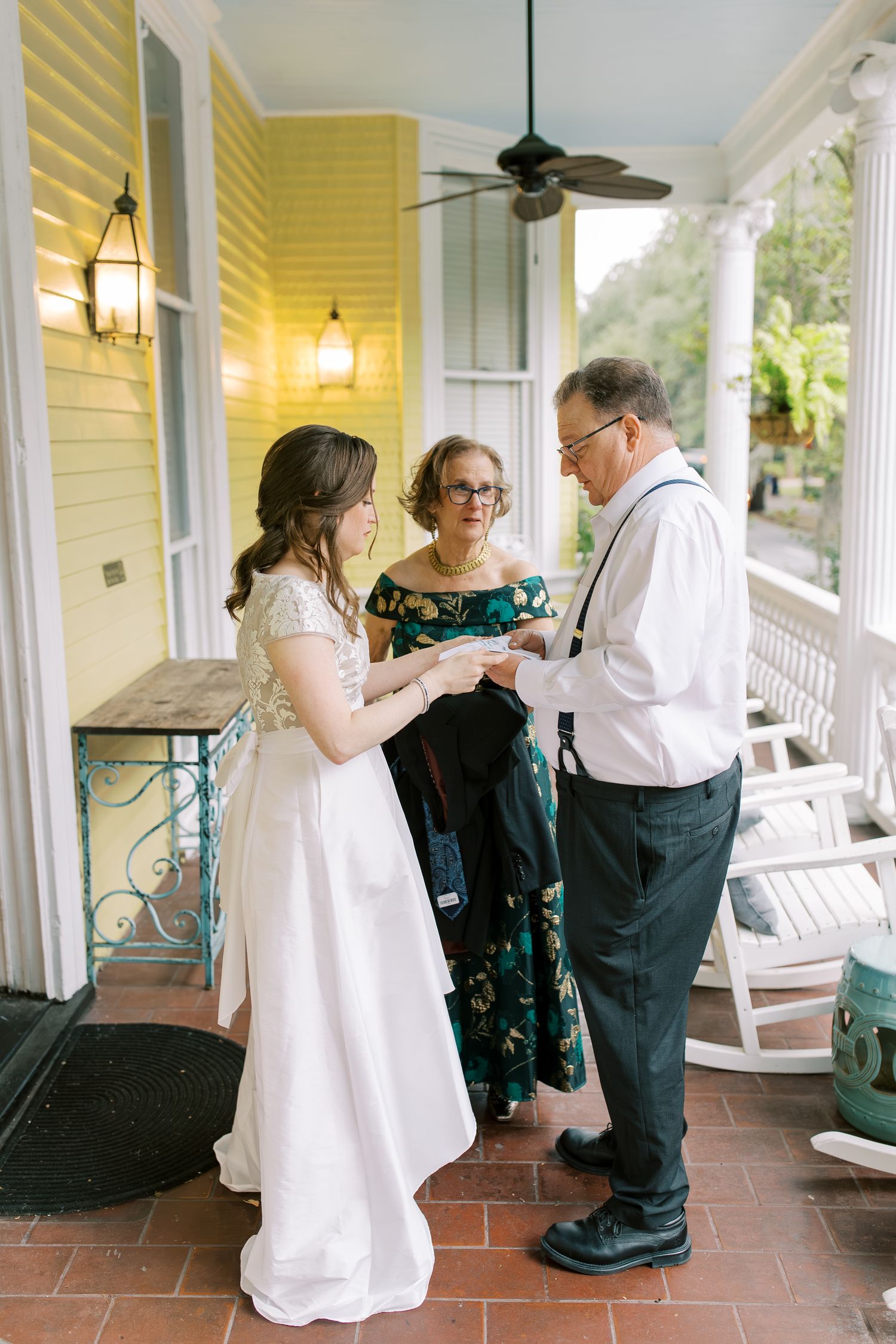 Wedding ceremony taking place on a yellow-walled porch with vintage lanterns and rocking chairs.