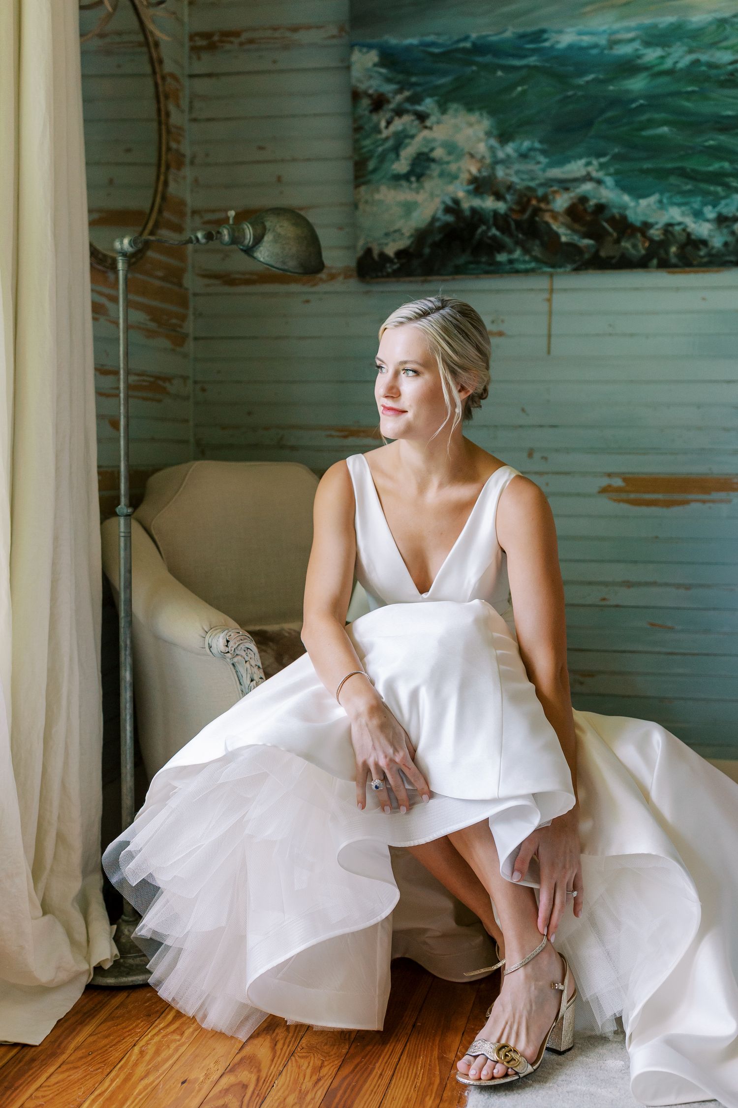 Bridal portrait in a coastal-themed room featuring a flowing white wedding gown and silver sandals in the Rose Cottage on Isle of Hope.