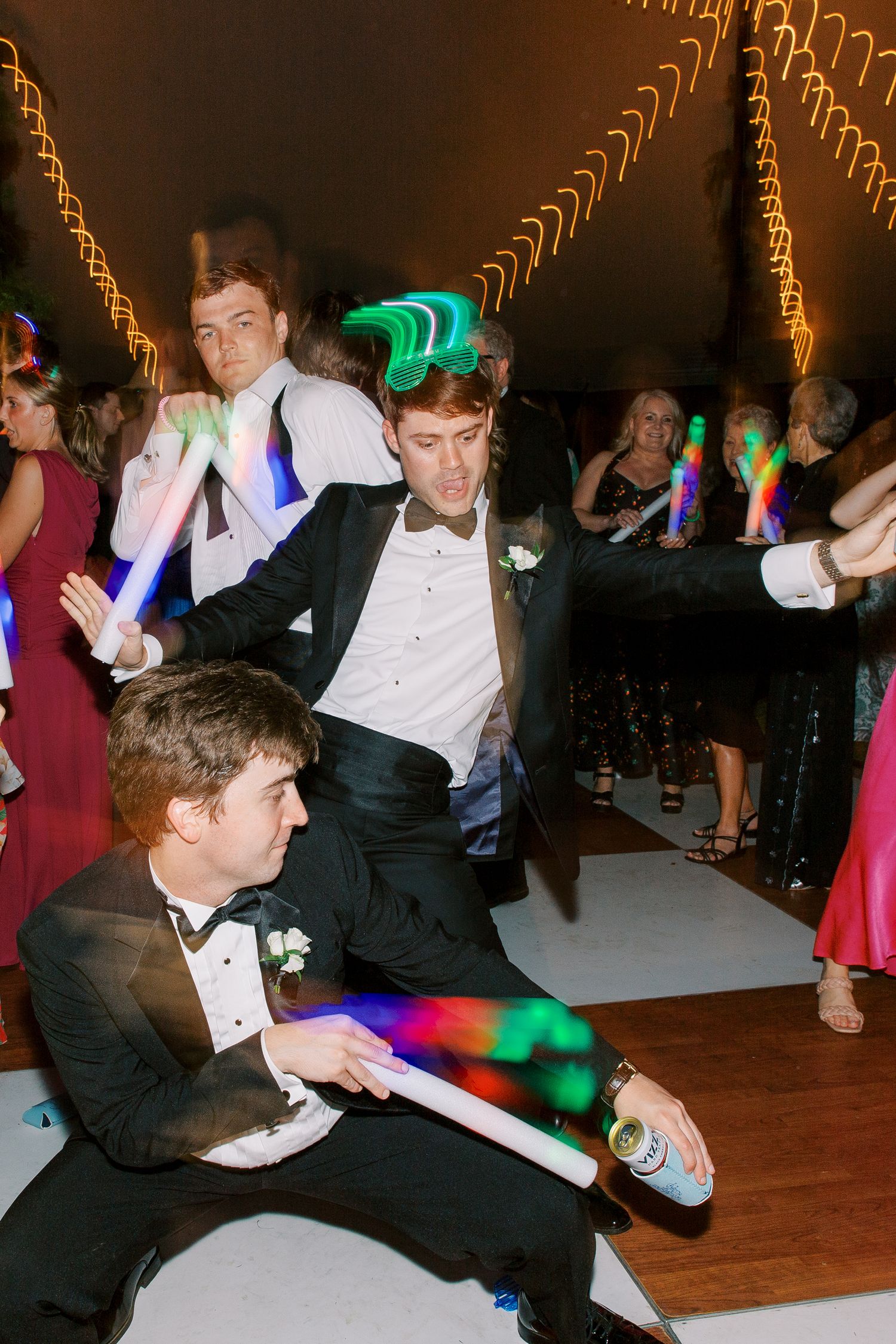 Wedding guests dancing at reception with colorful lights and formal attire.