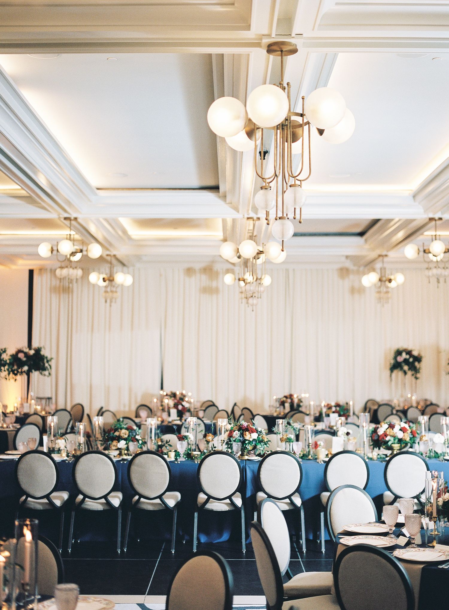 Elegant ballroom setup at Perry Lane Hotel with white and navy blue decor featuring round tables and classic chandeliers overhead.