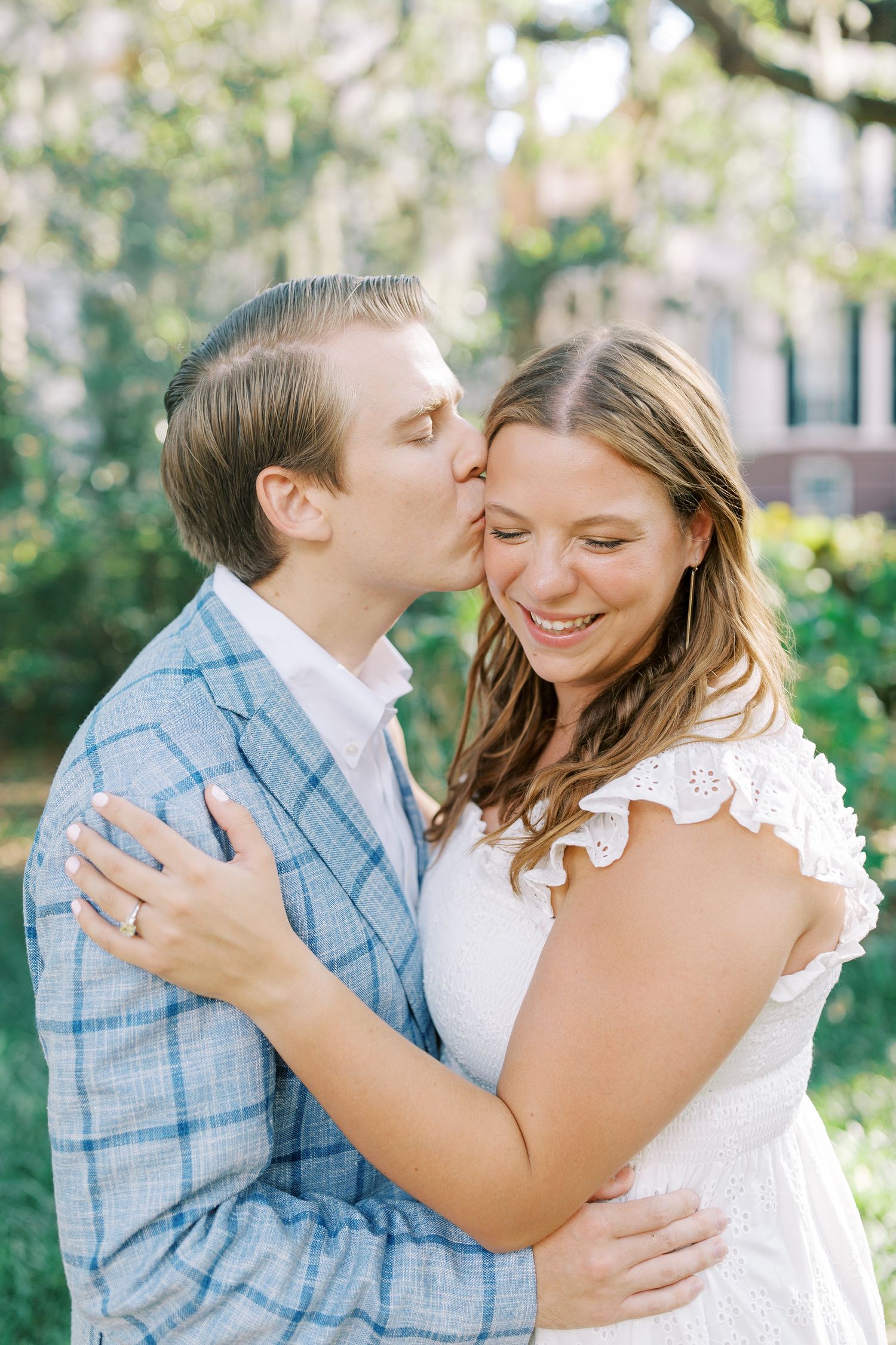 Sweet romantic moment captured outdoors with a gentle forehead kiss between a couple dressed in blue and white.