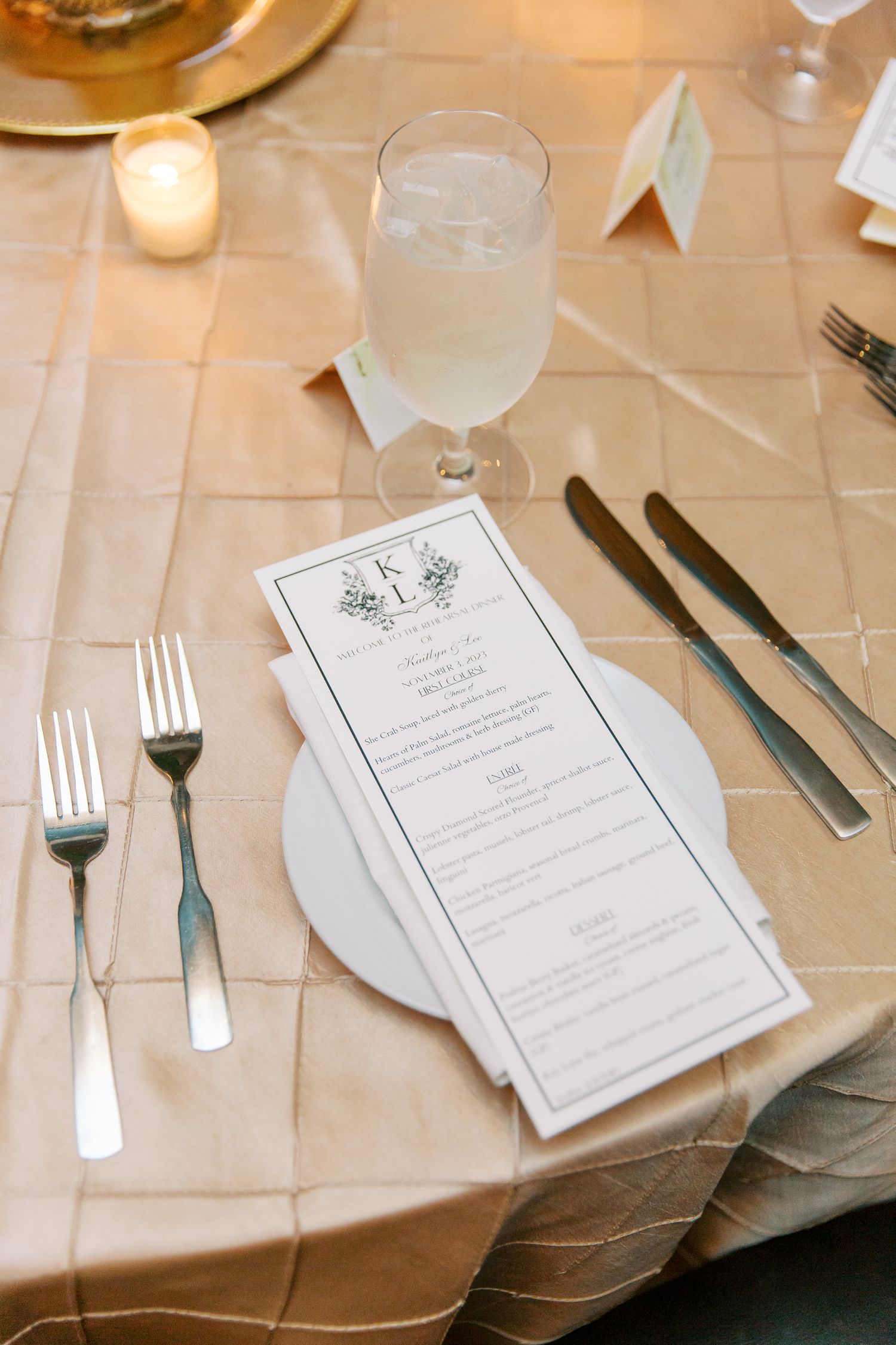 Elegant table setting with menu card, silverware and water glass on beige tablecloth at upscale restaurant.