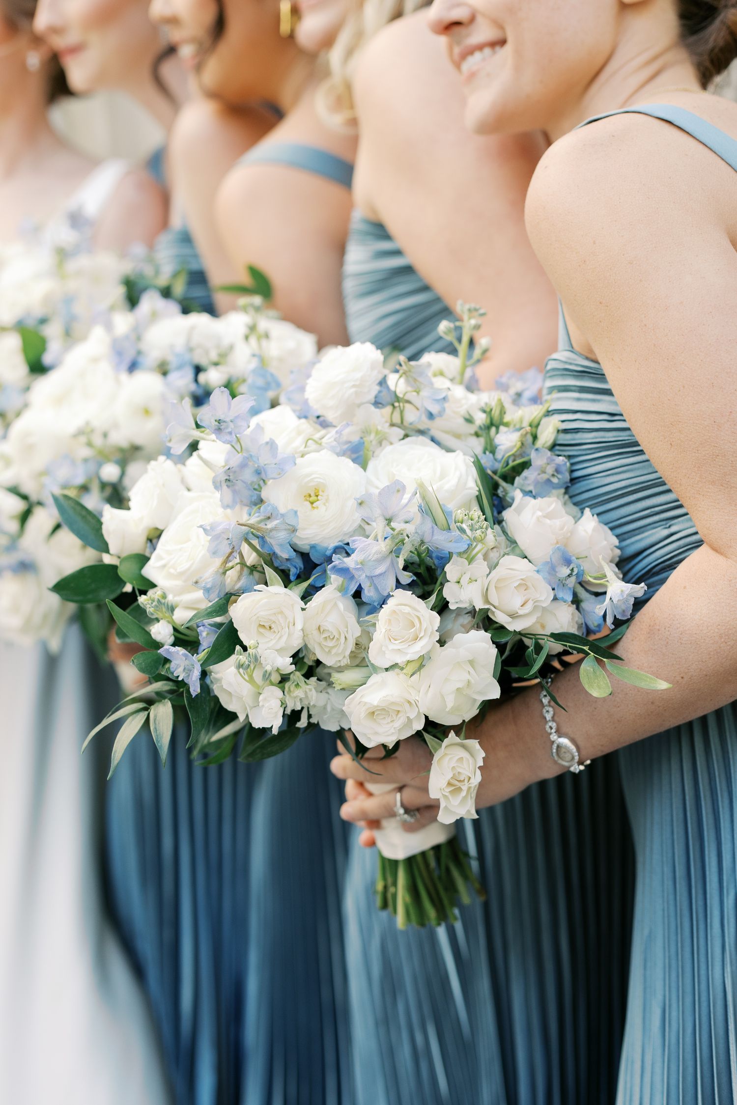 Bridesmaids in dusty blue dresses holding white and blue floral bouquets.