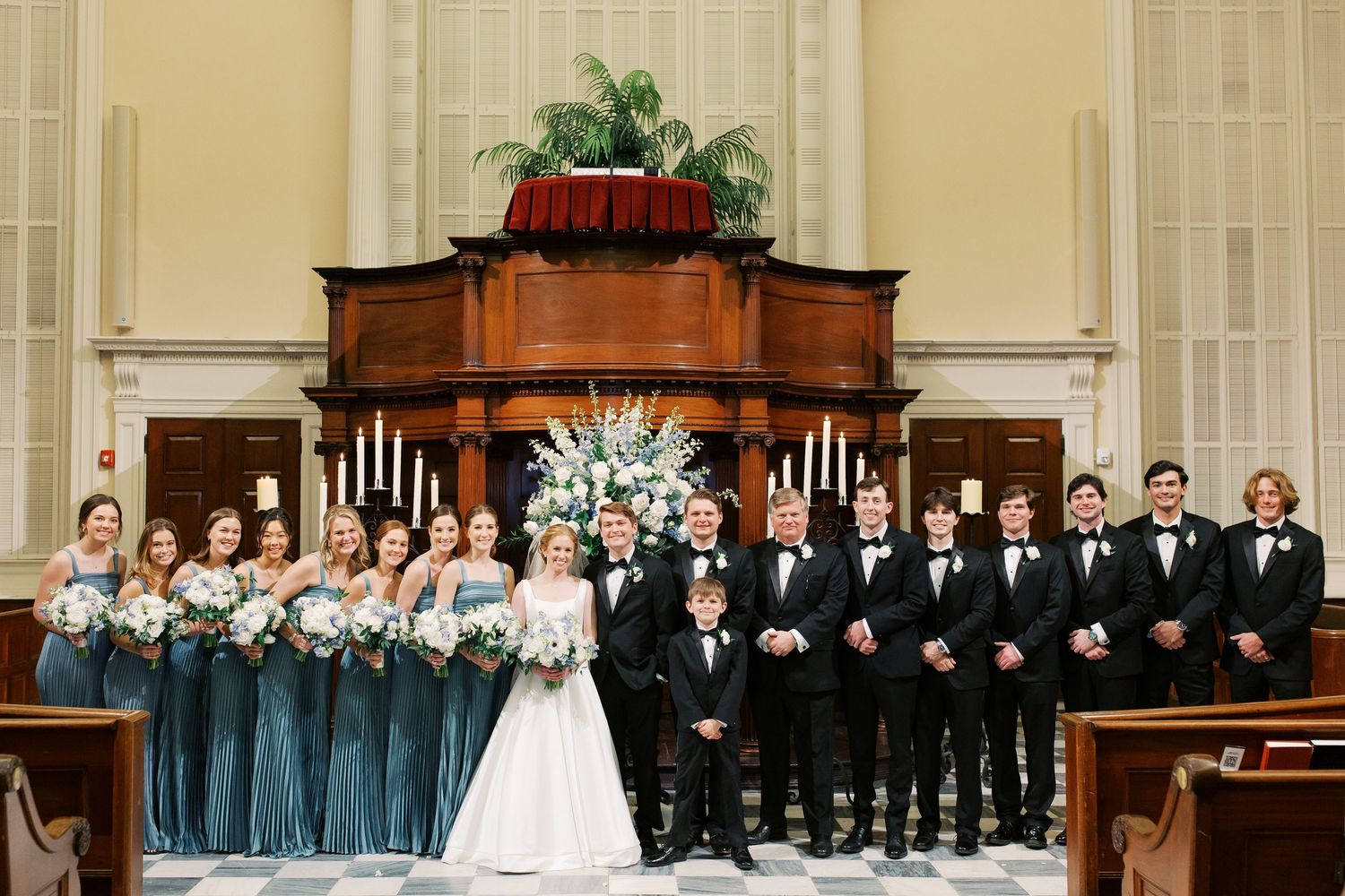 Wedding party lined up in church with bridesmaids in blue and groomsmen in black.