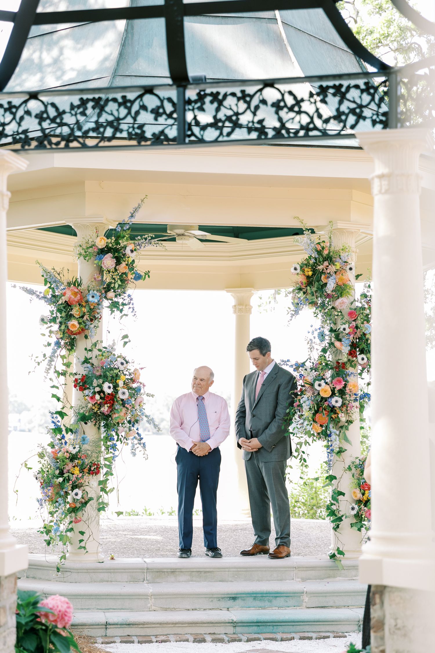 Wedding ceremony setup in white gazebo decorated with colorful floral arrangements.