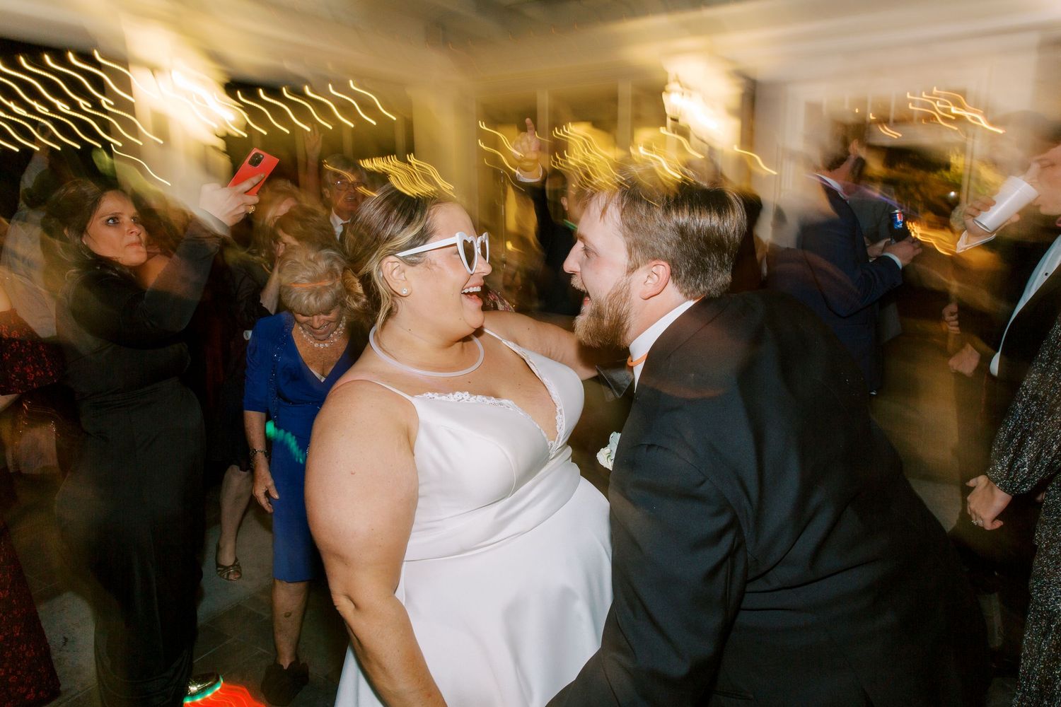 A bride and groom dancing and laughing together on a lively wedding reception dance floor.