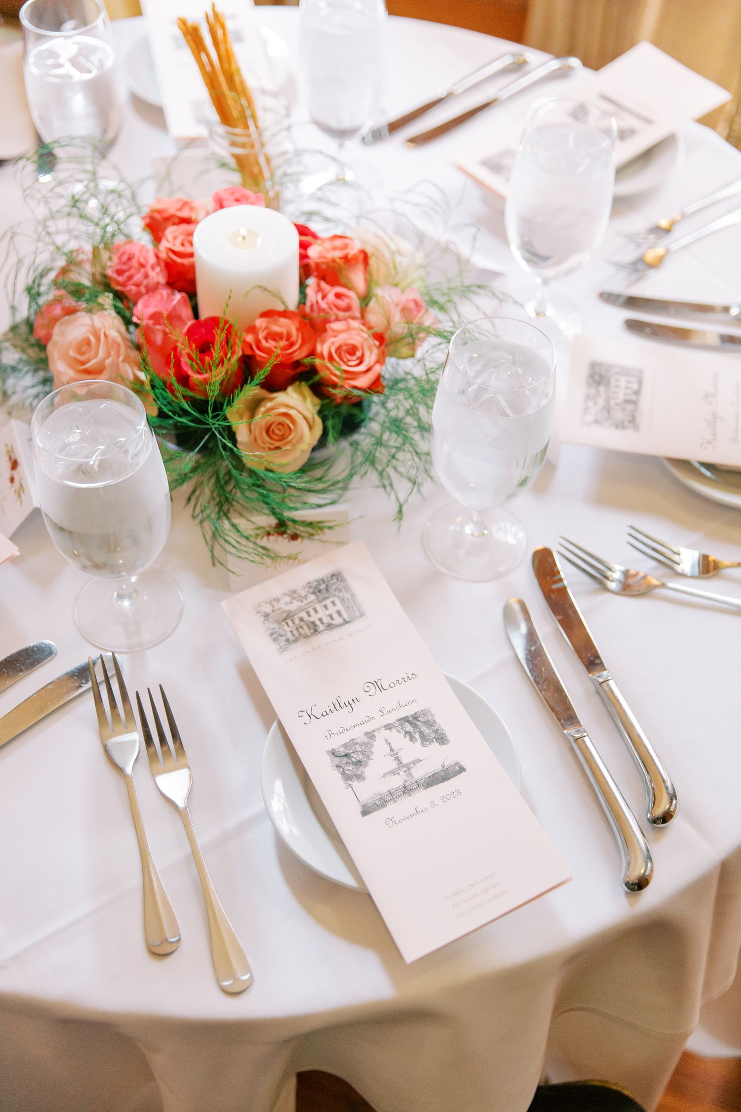 Elegant table setting with peach roses centerpiece, white linens, and formal place settings at a wedding reception.