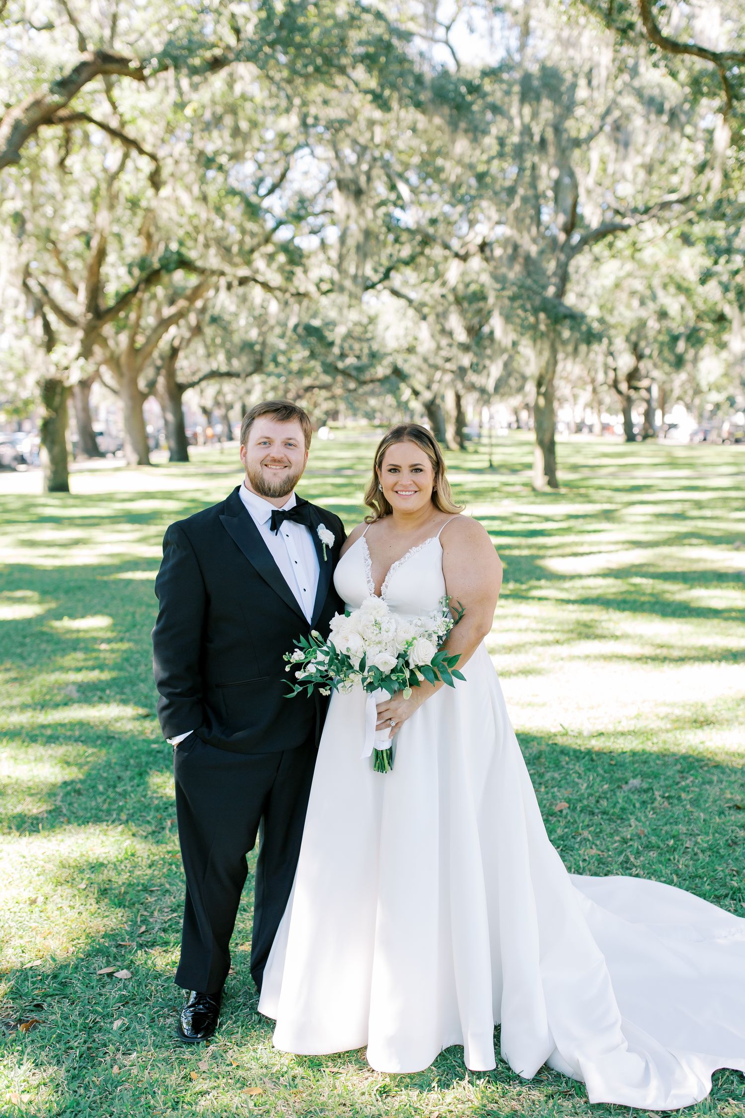 Newlyweds pose for portrait under Spanish moss trees in a park setting.
