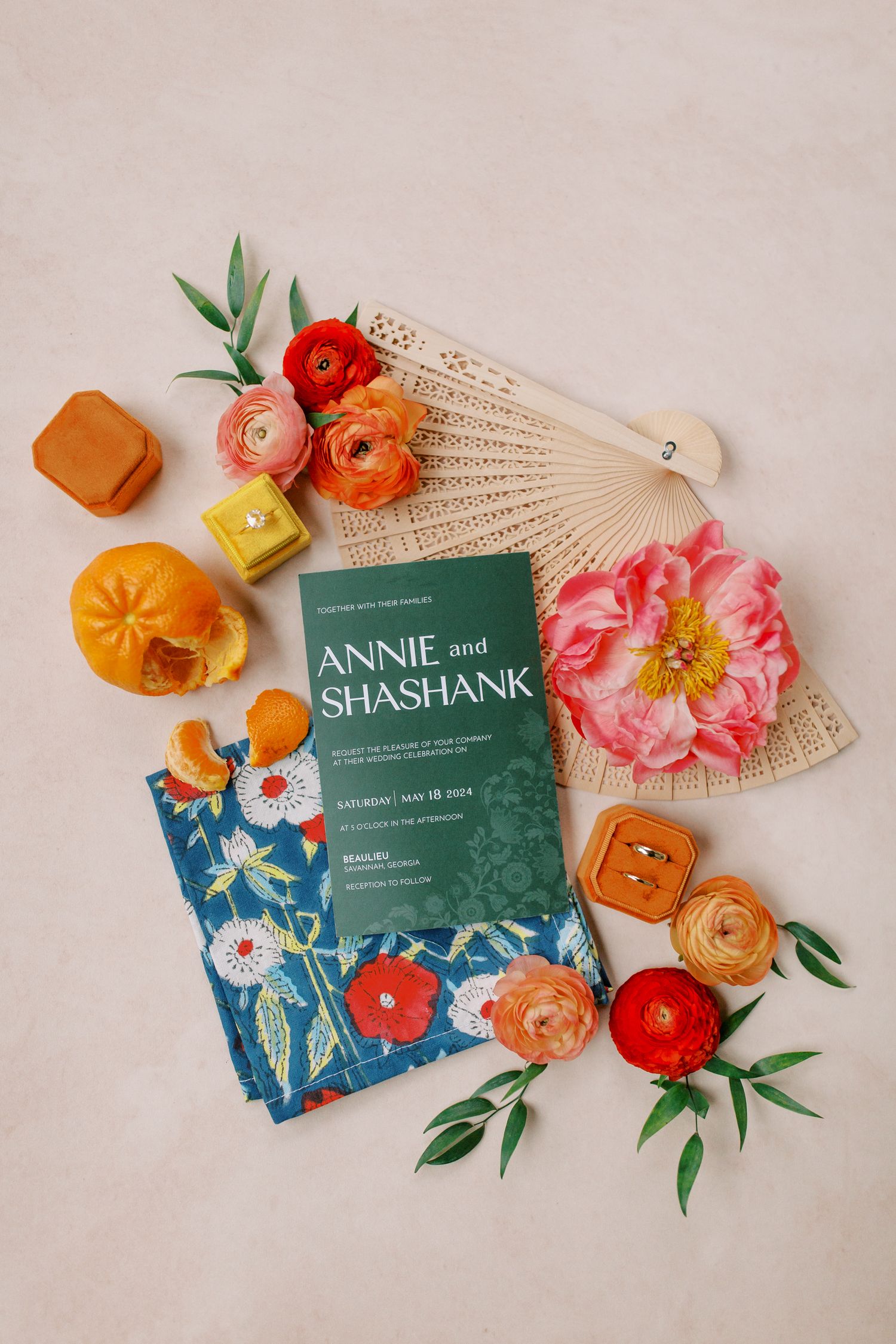 Wedding invitation styled with coral flowers, fan and orange decor elements on beige background.