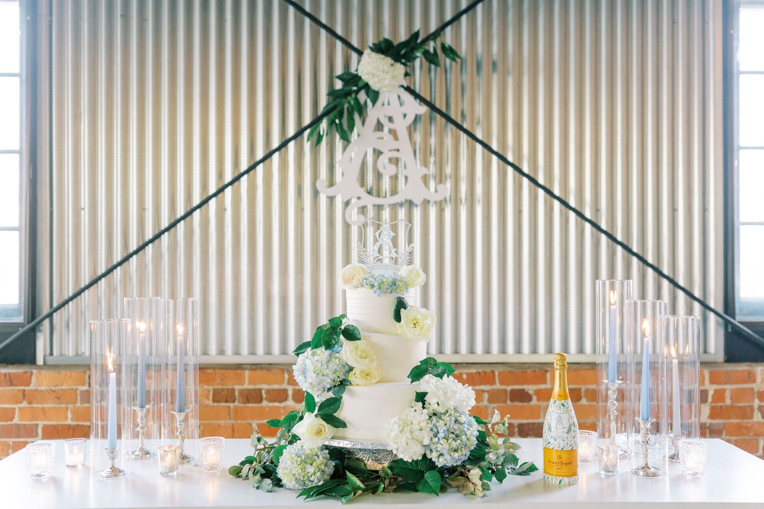 Three-tiered white wedding cake displayed with crystal chandelier and floral decorations at the Kehoe Ironworks Building.