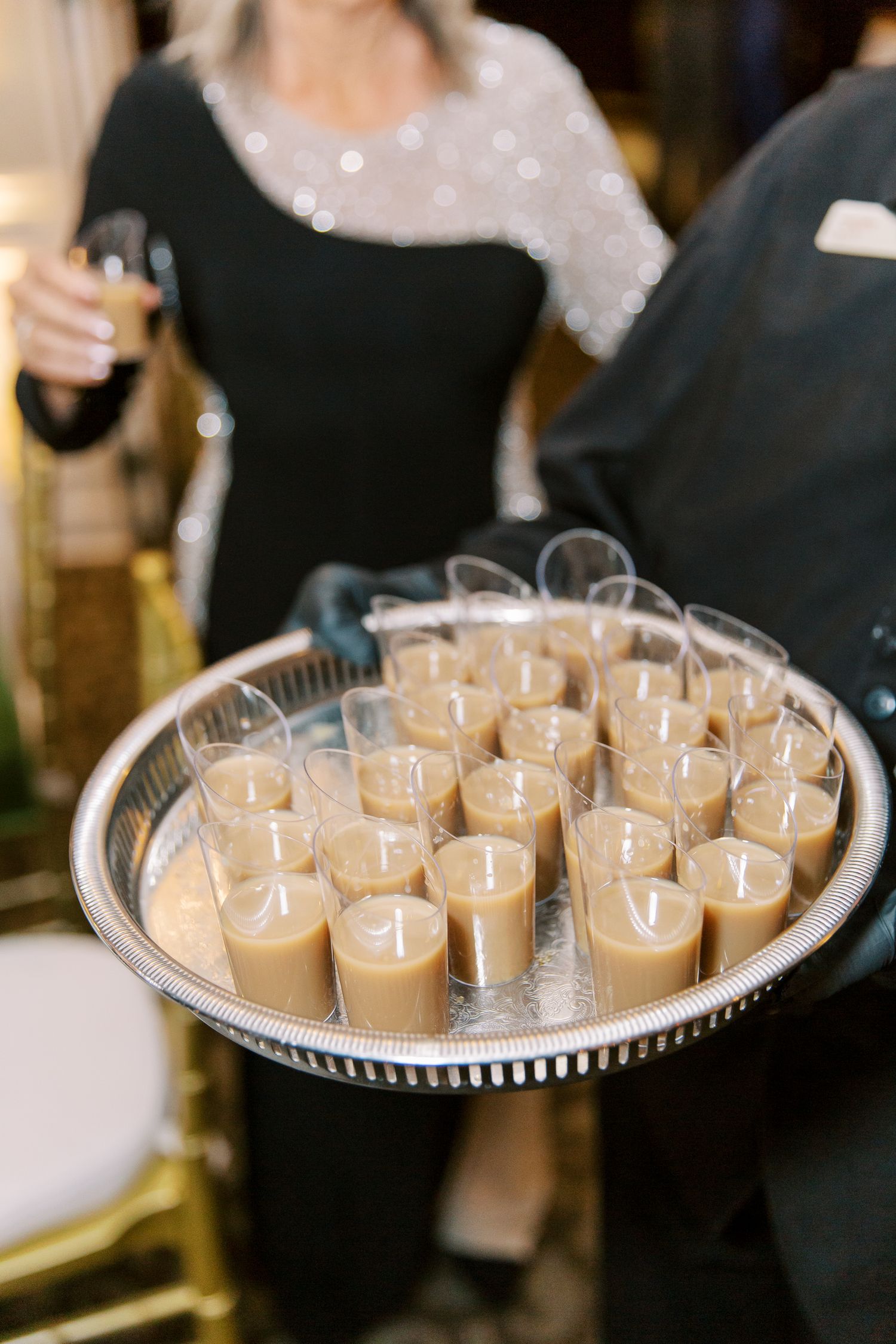 Silver tray filled with caramel-colored dessert shooters being served at an event.