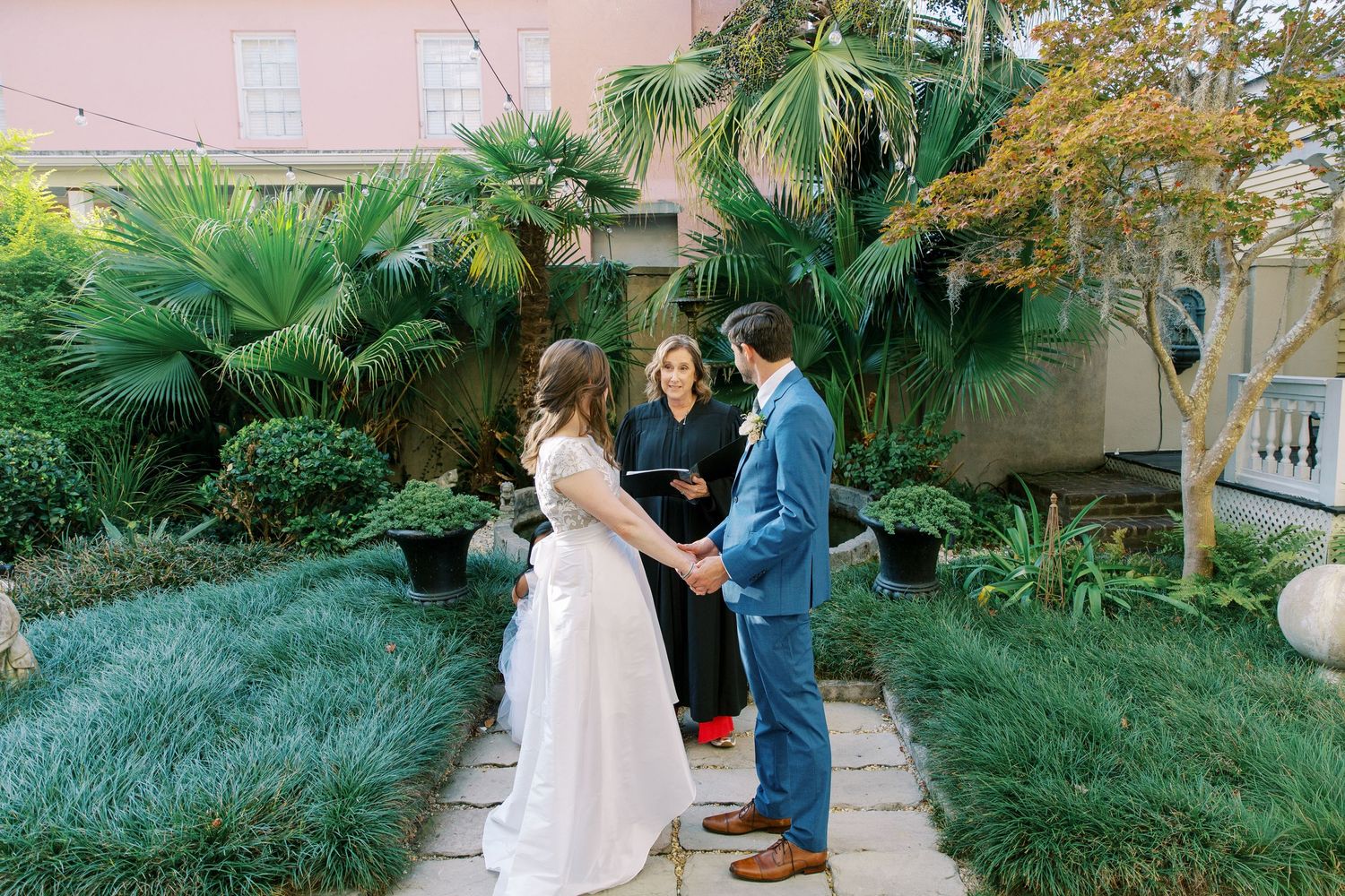 Outdoor wedding ceremony taking place among lush garden greenery and palm trees.