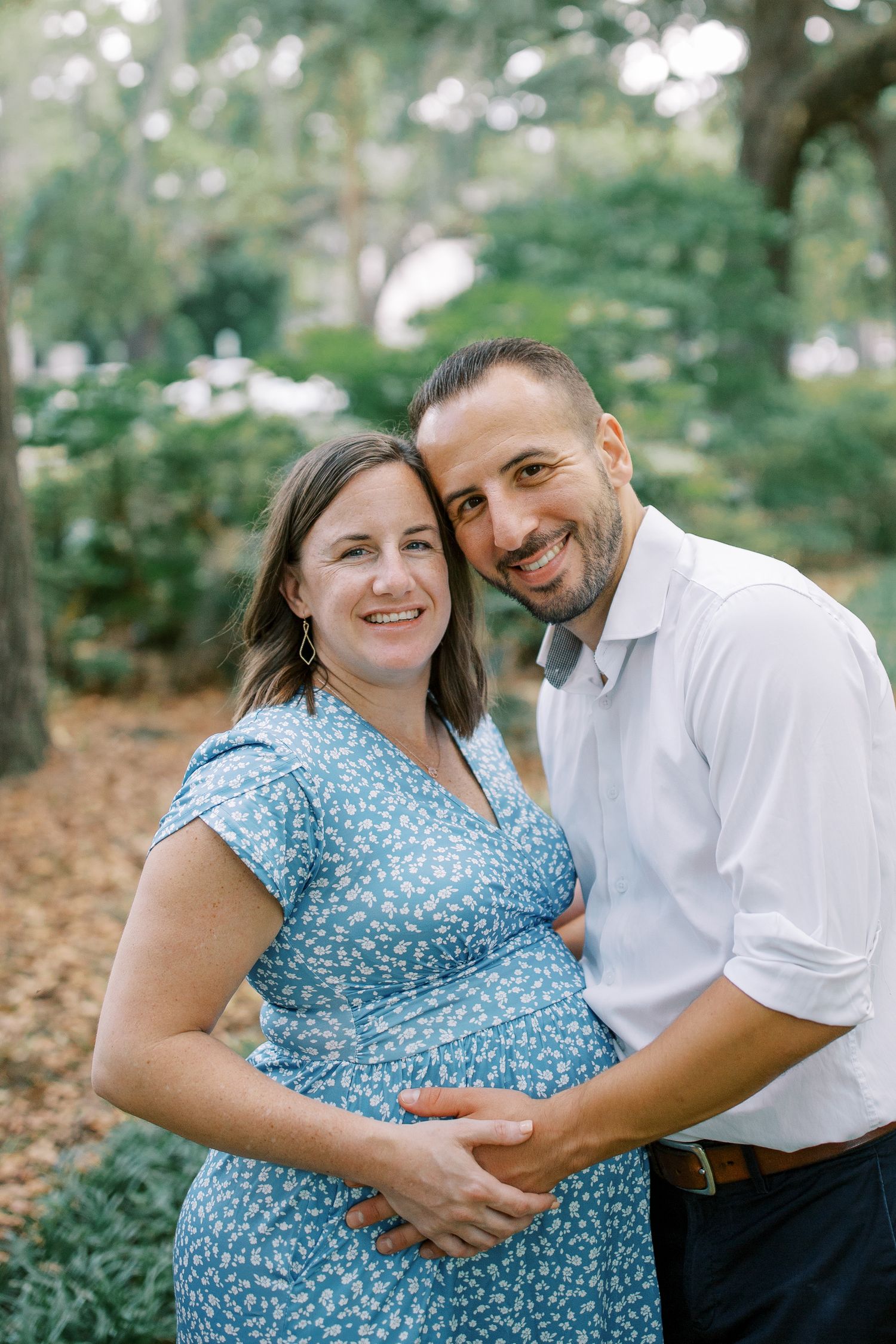 Romantic couple embraces outdoors with woman in blue polka dot dress and man in white shirt.