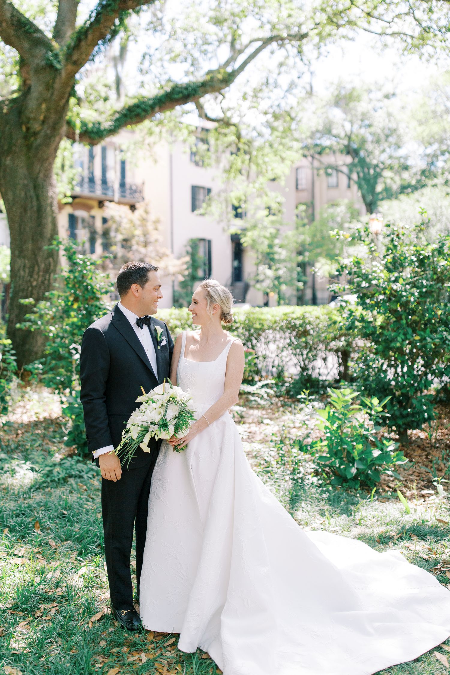 Elegant wedding couple standing among Spanish moss trees in a garden setting.