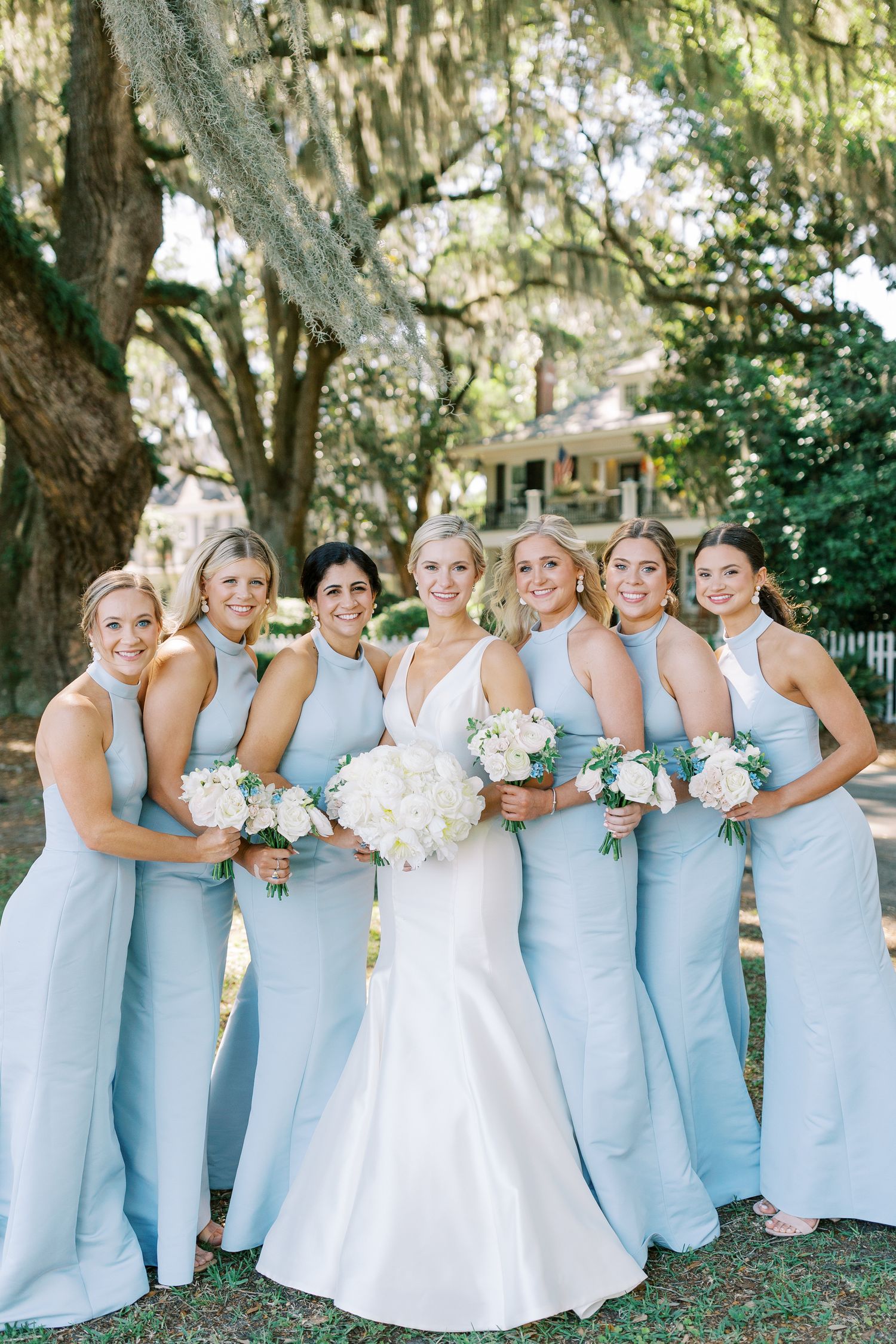 Wedding party in light blue dresses poses outdoors under Spanish moss draped trees on Bluff Drive in Isle of Hope.
