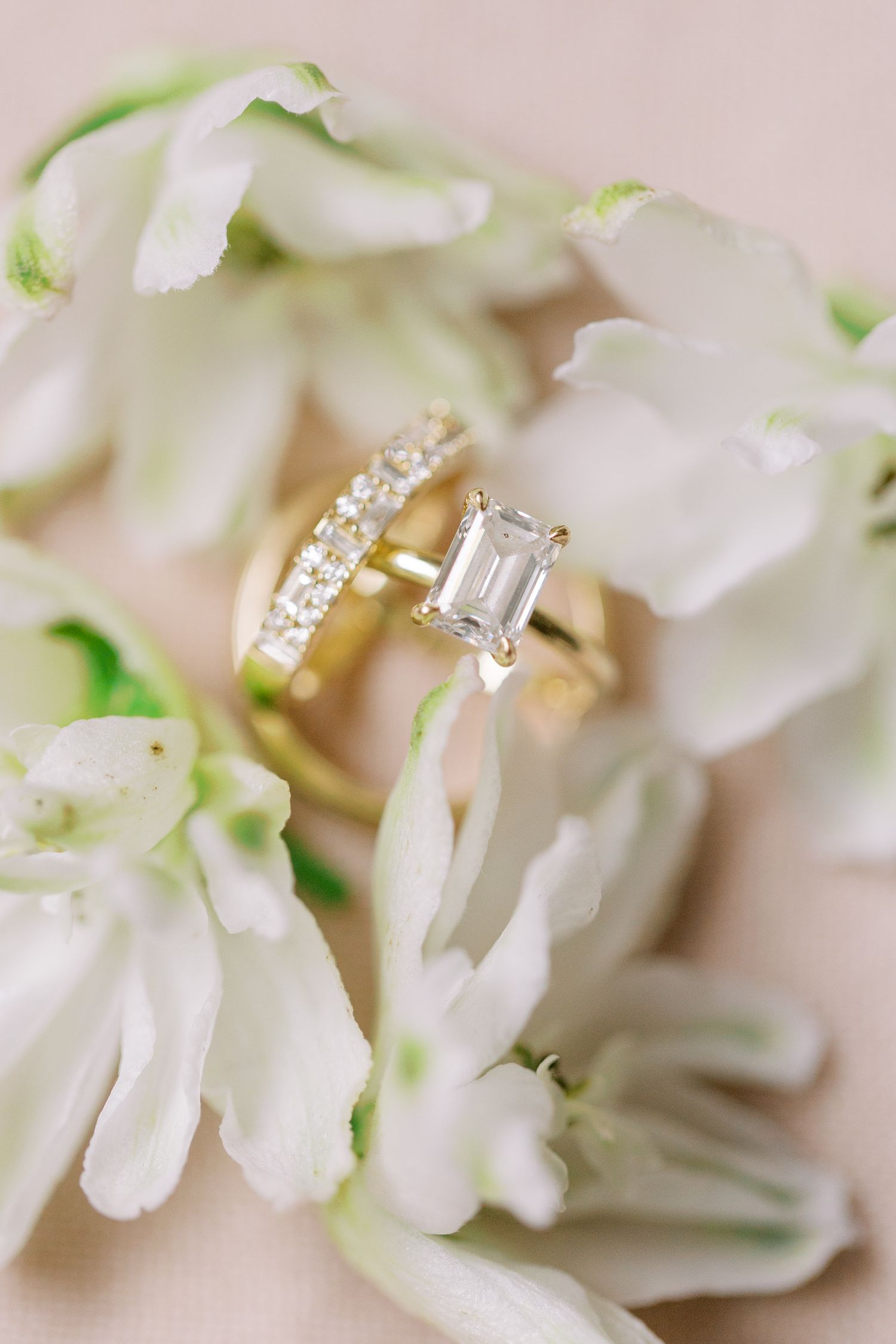 Diamond engagement ring and wedding band nestled among white flowers.