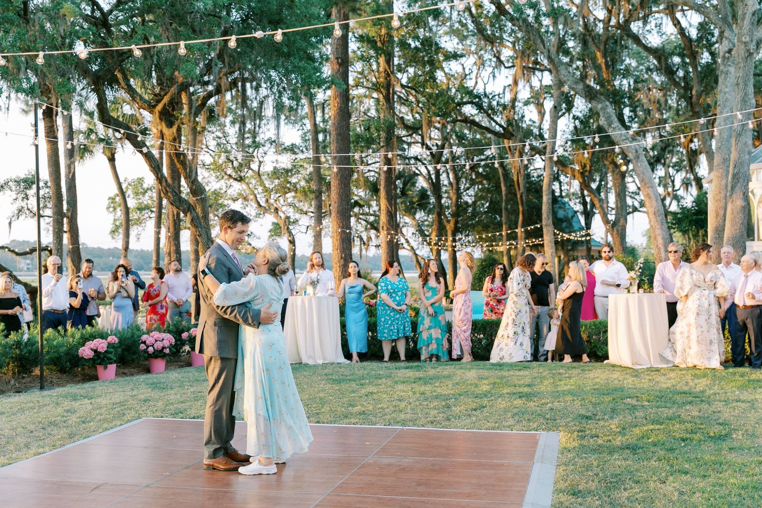 Outdoor evening wedding reception with couples dancing on wooden dance floor.