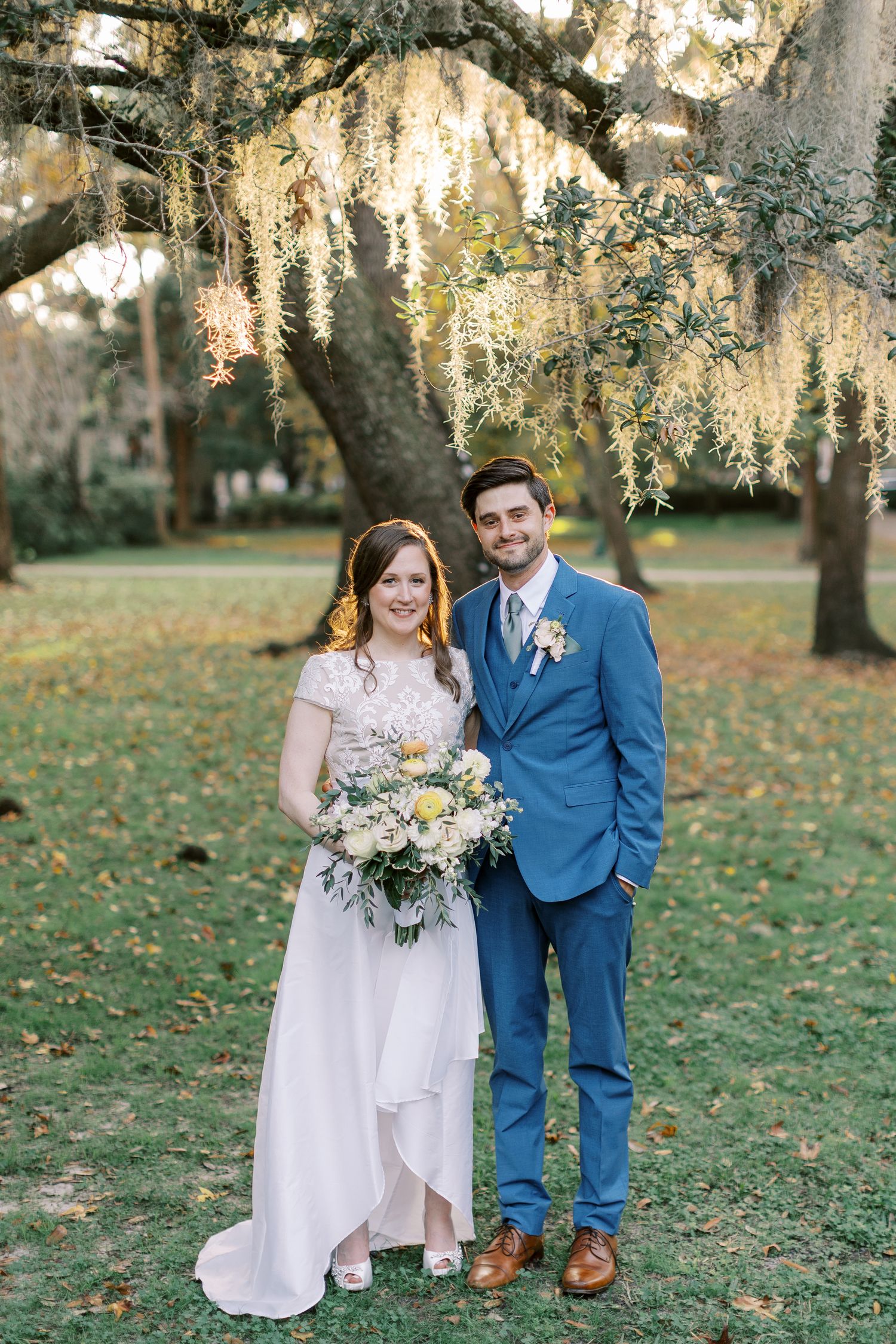 A wedding portrait under Spanish moss draped trees in a scenic park setting.