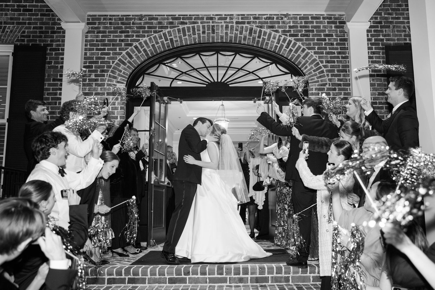 Wedding exit through brick archway as guests shower couple with confetti.