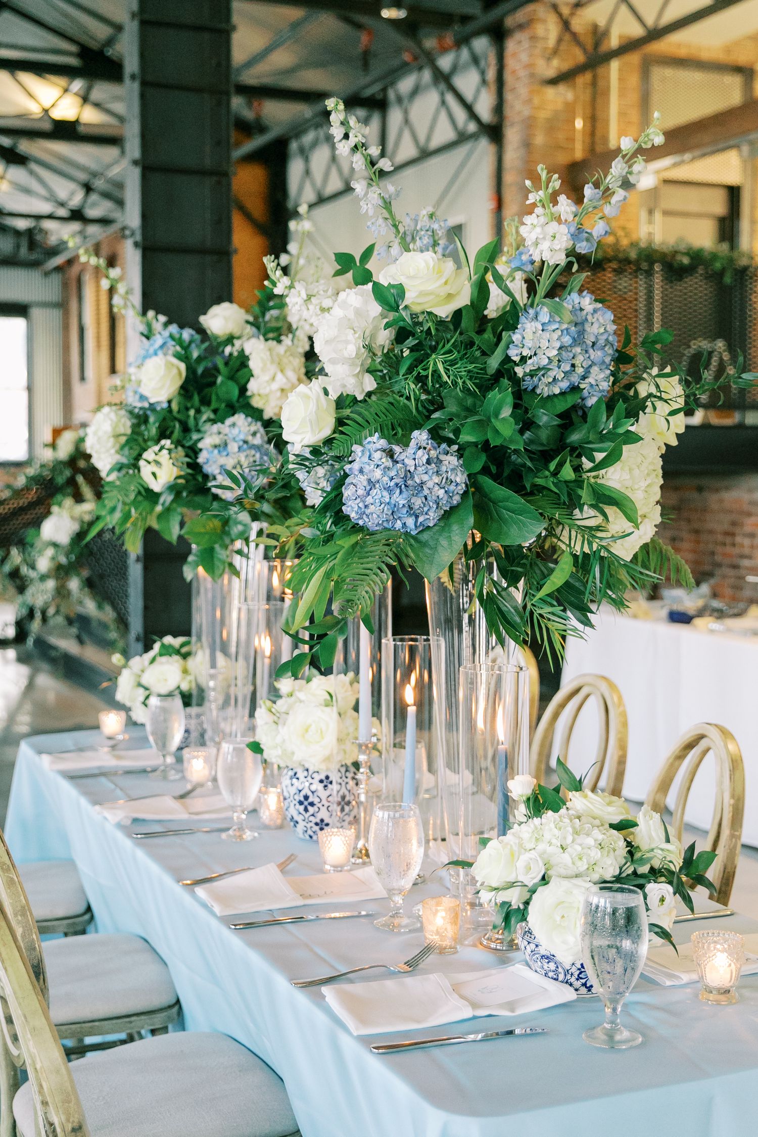Elegant table setting with blue and white floral centerpiece, crystal glassware and gold chairs.