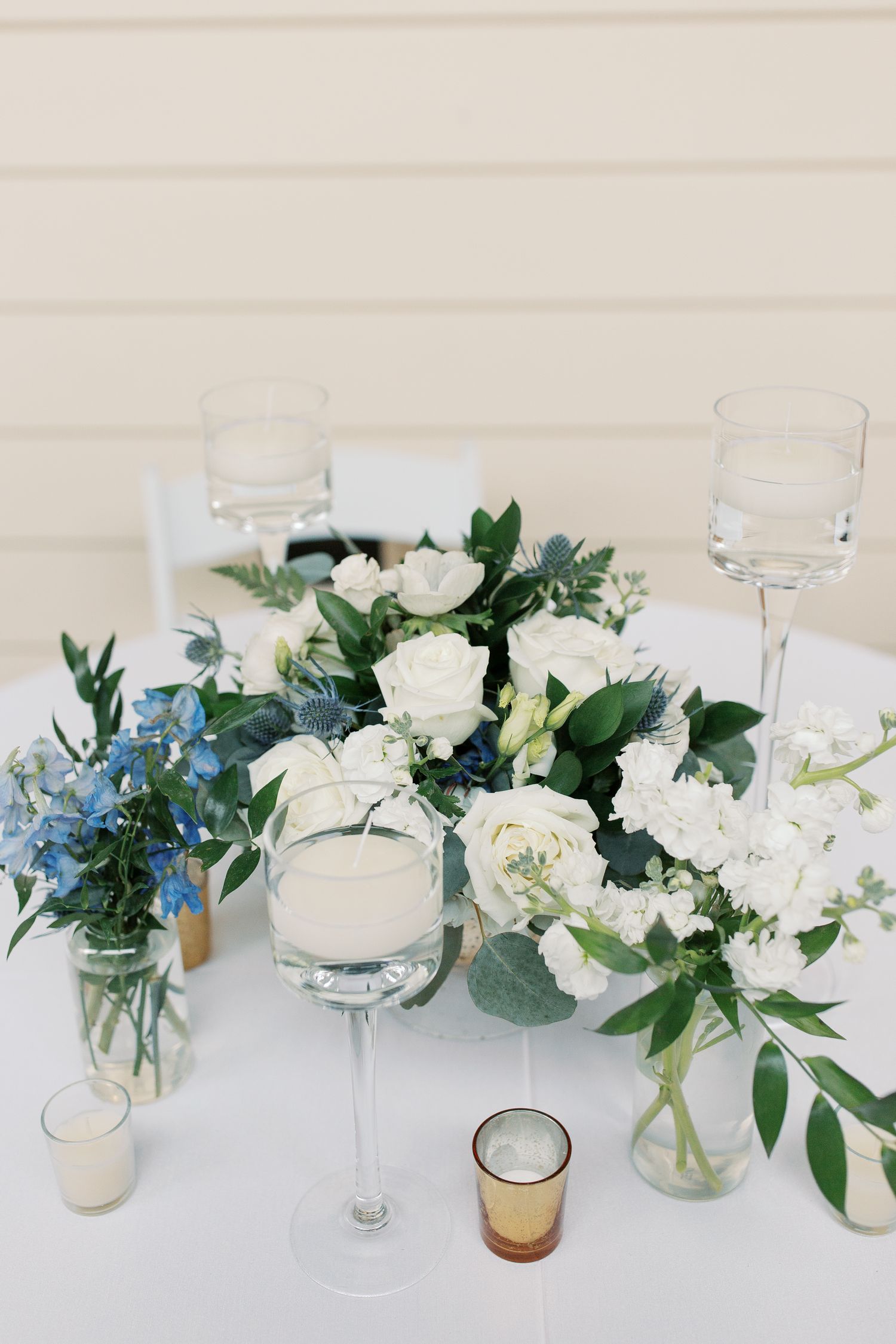 White and blue floral centerpiece arrangements with greenery displayed on white tablecloths.