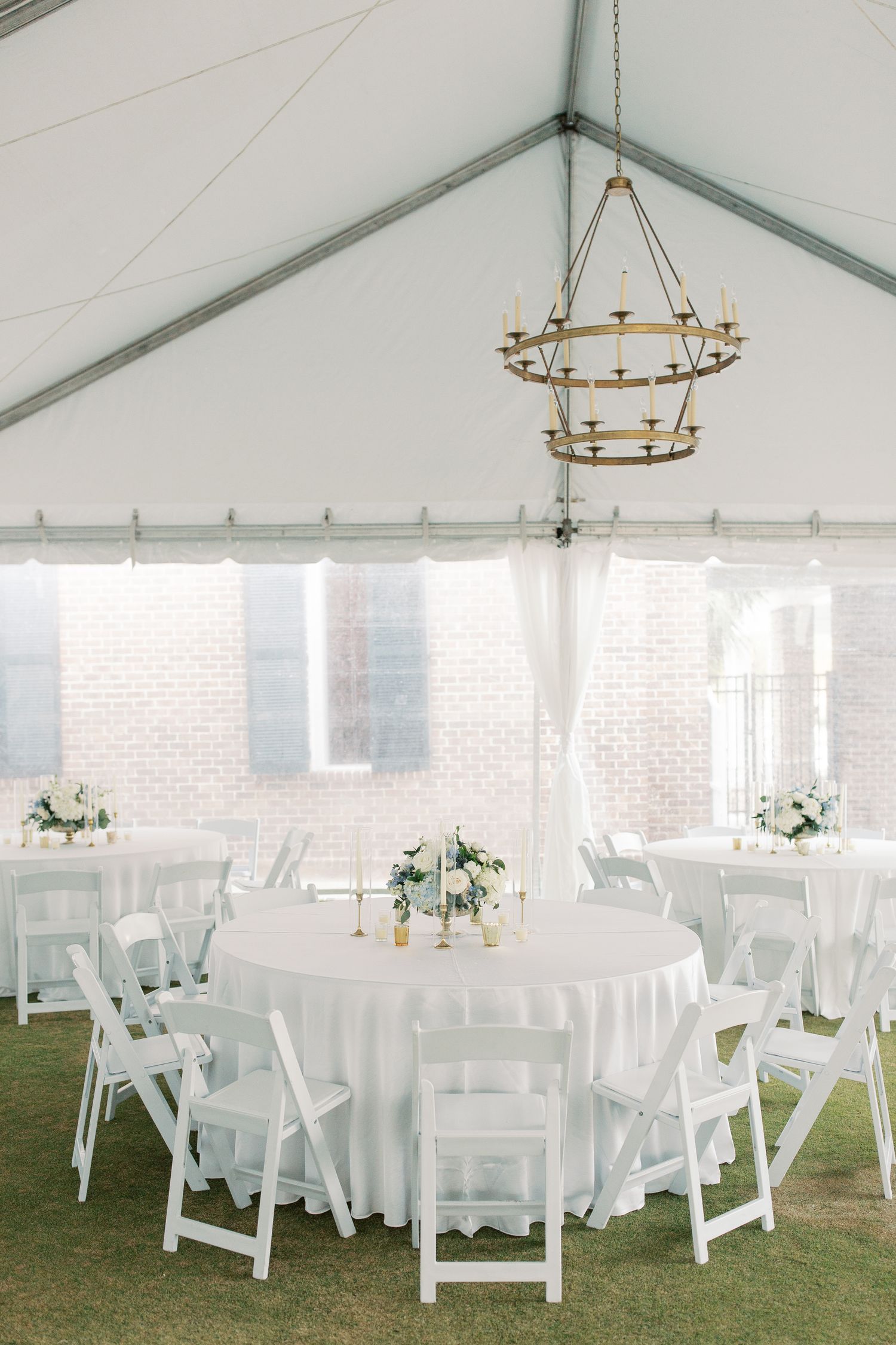 Elegant white wedding reception tent with round tables, white chairs and tiered chandelier.