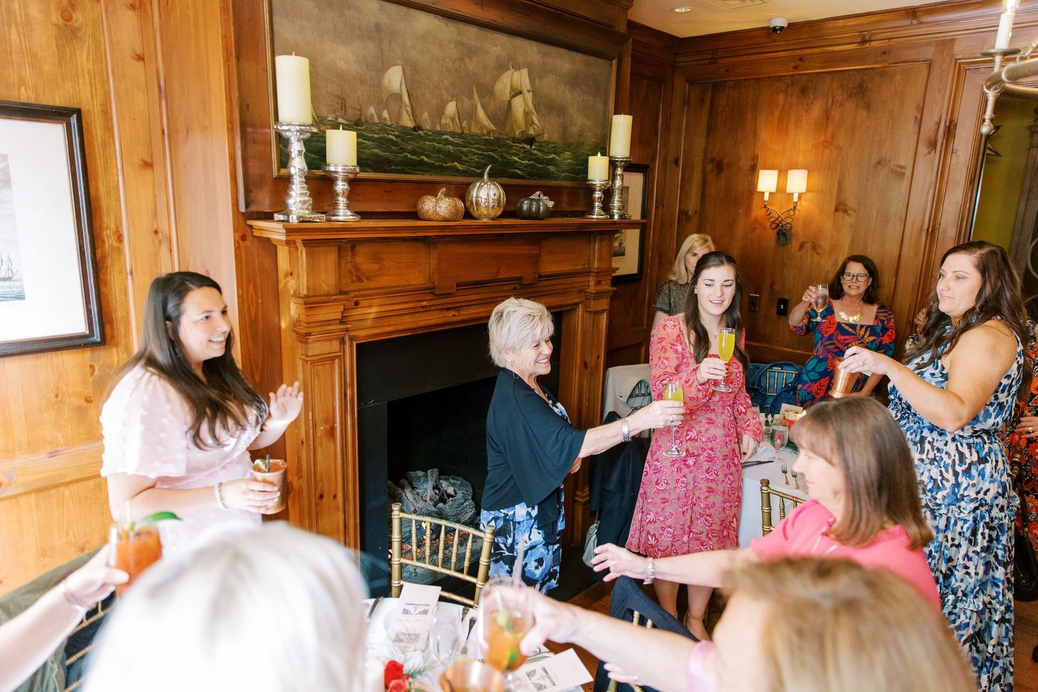 Party guests gather in a wood-paneled room with a fireplace for a festive celebration.