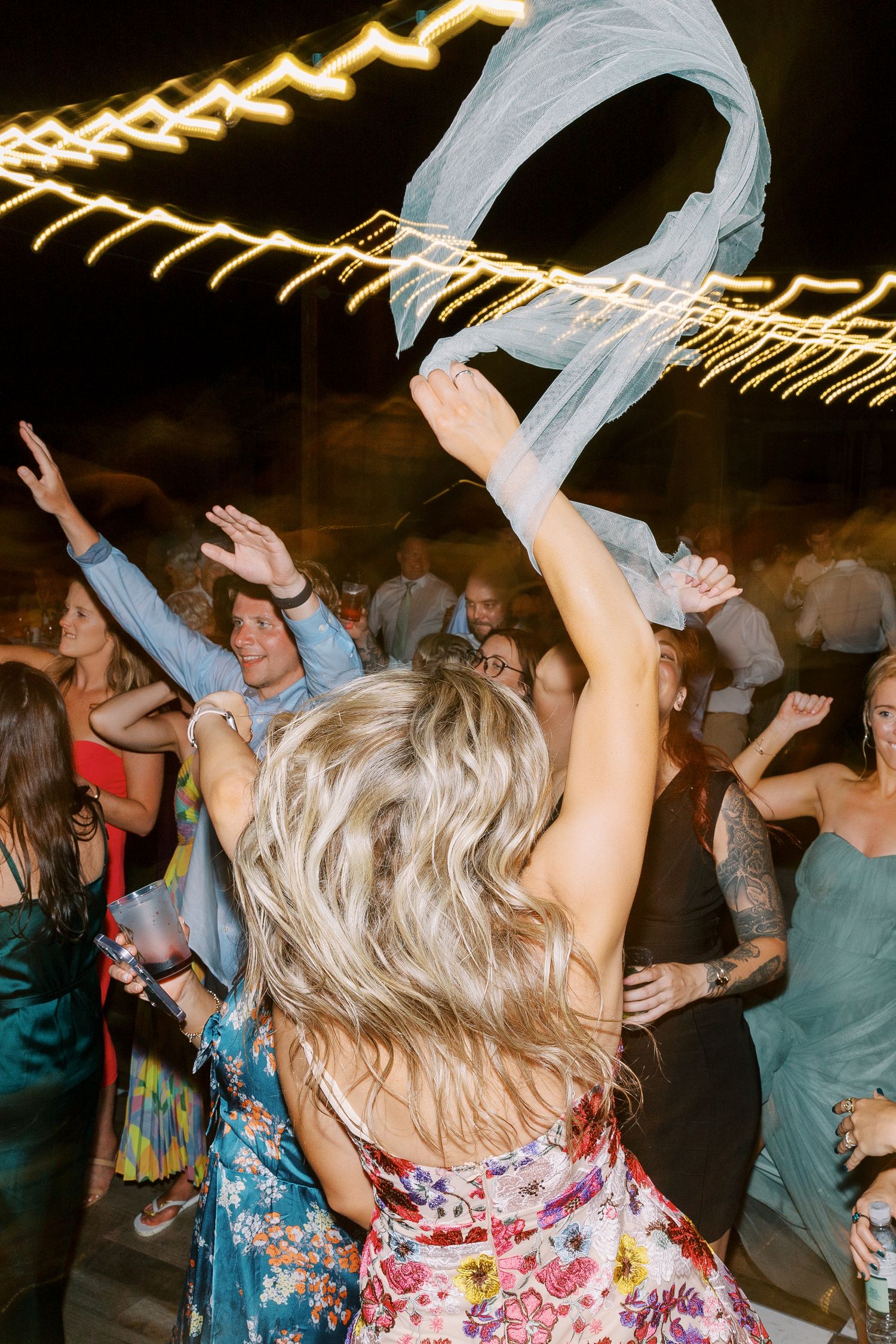 Wedding reception guests dancing and celebrating under glowing string lights.