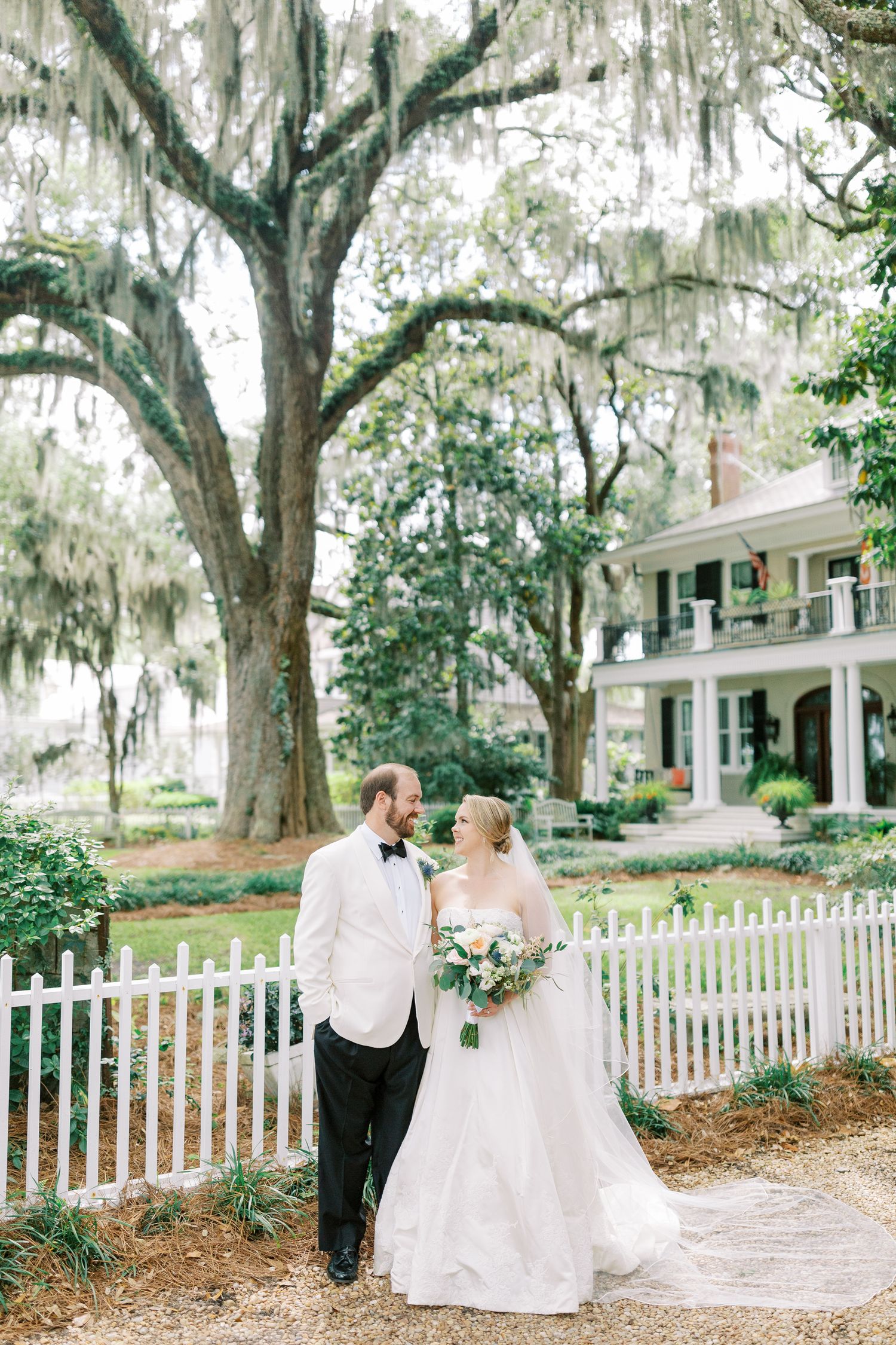 Southern wedding portrait in front of historic mansion with Spanish moss draped trees.
