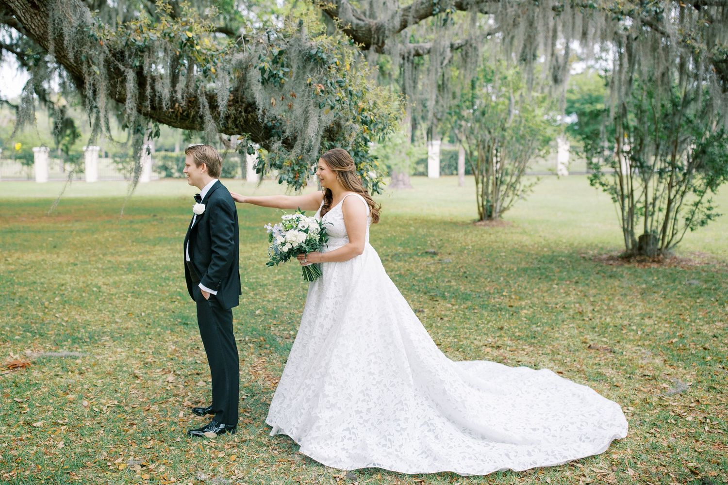First look wedding moment under Spanish moss trees in a Southern garden.
