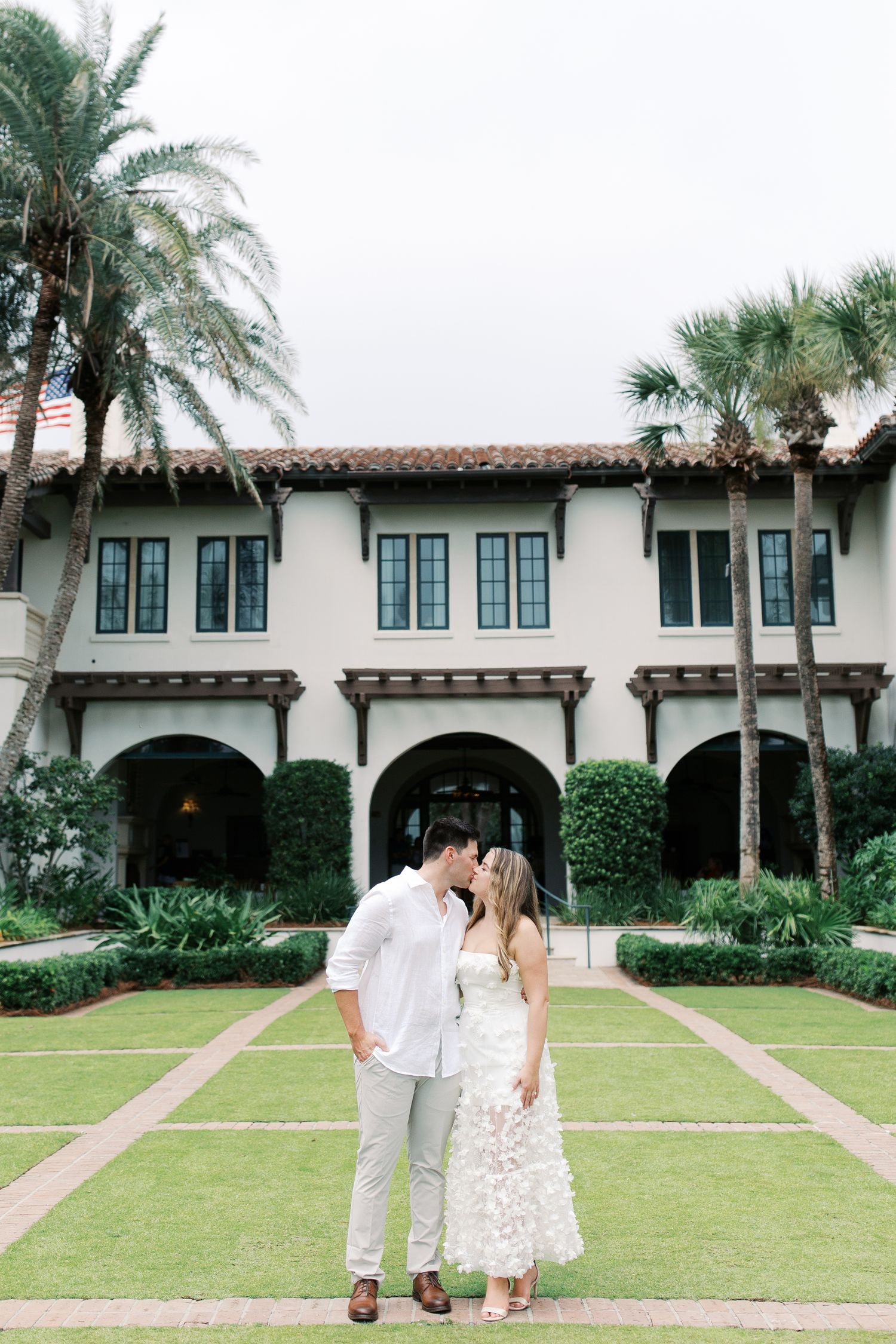Couple standing on lawn in front of Mediterranean style building with palm trees at Sea Island in St. Simons.