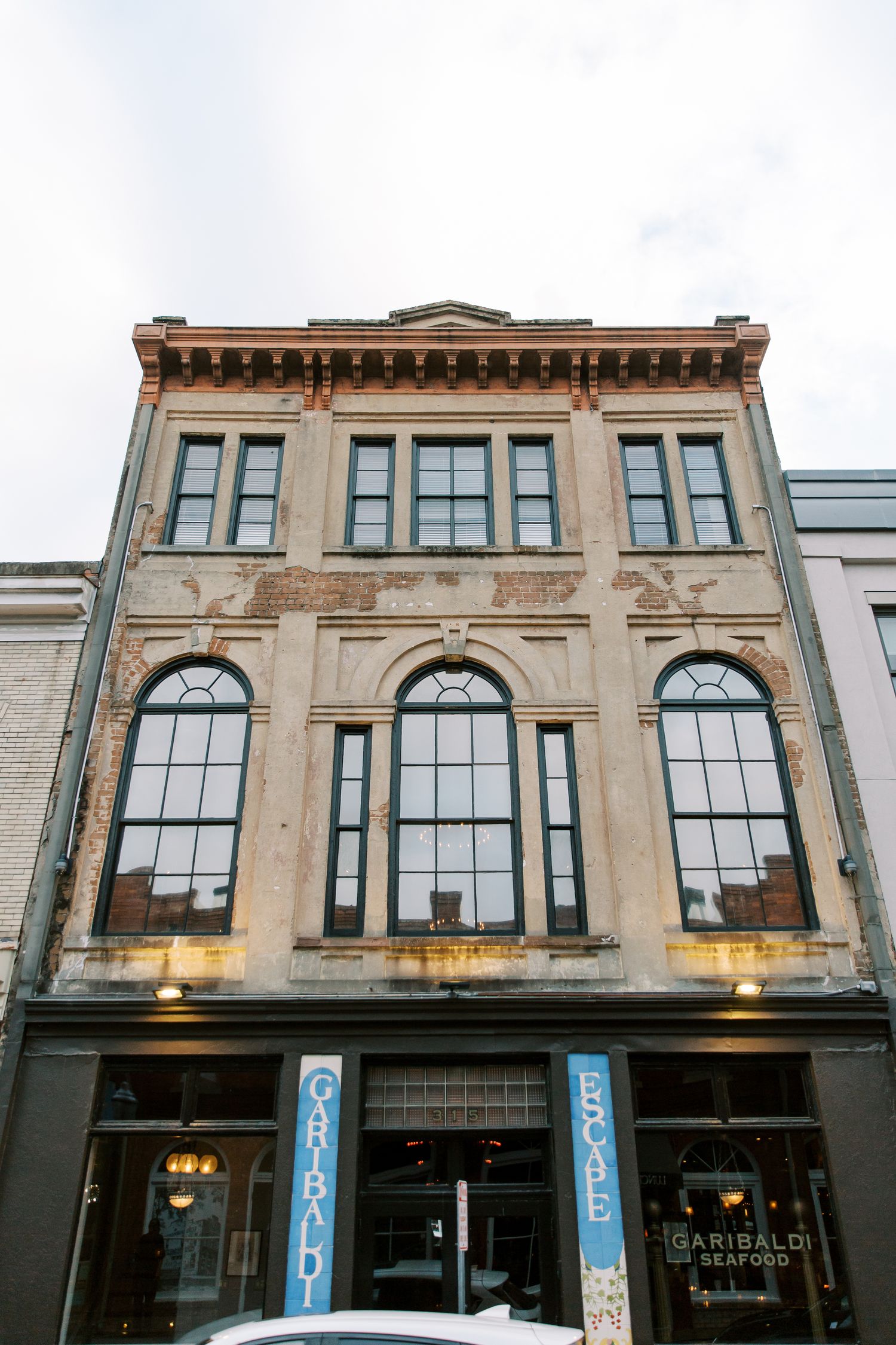 Historic three-story beige stone building with ornate arched windows and decorative cornice on a city street.