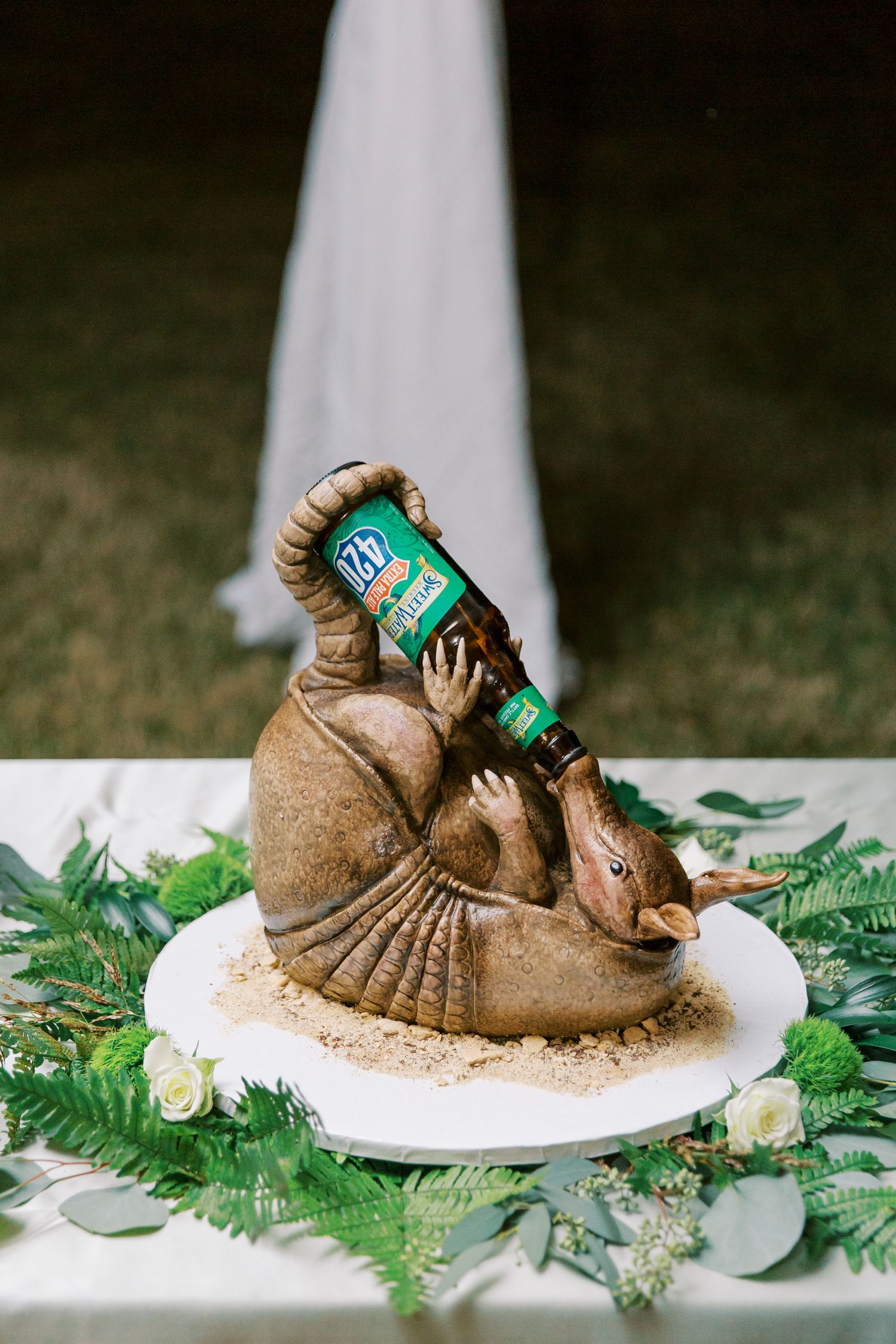 Unique wedding cake topper featuring bronze seal drinking from a bottle surrounded by greenery.